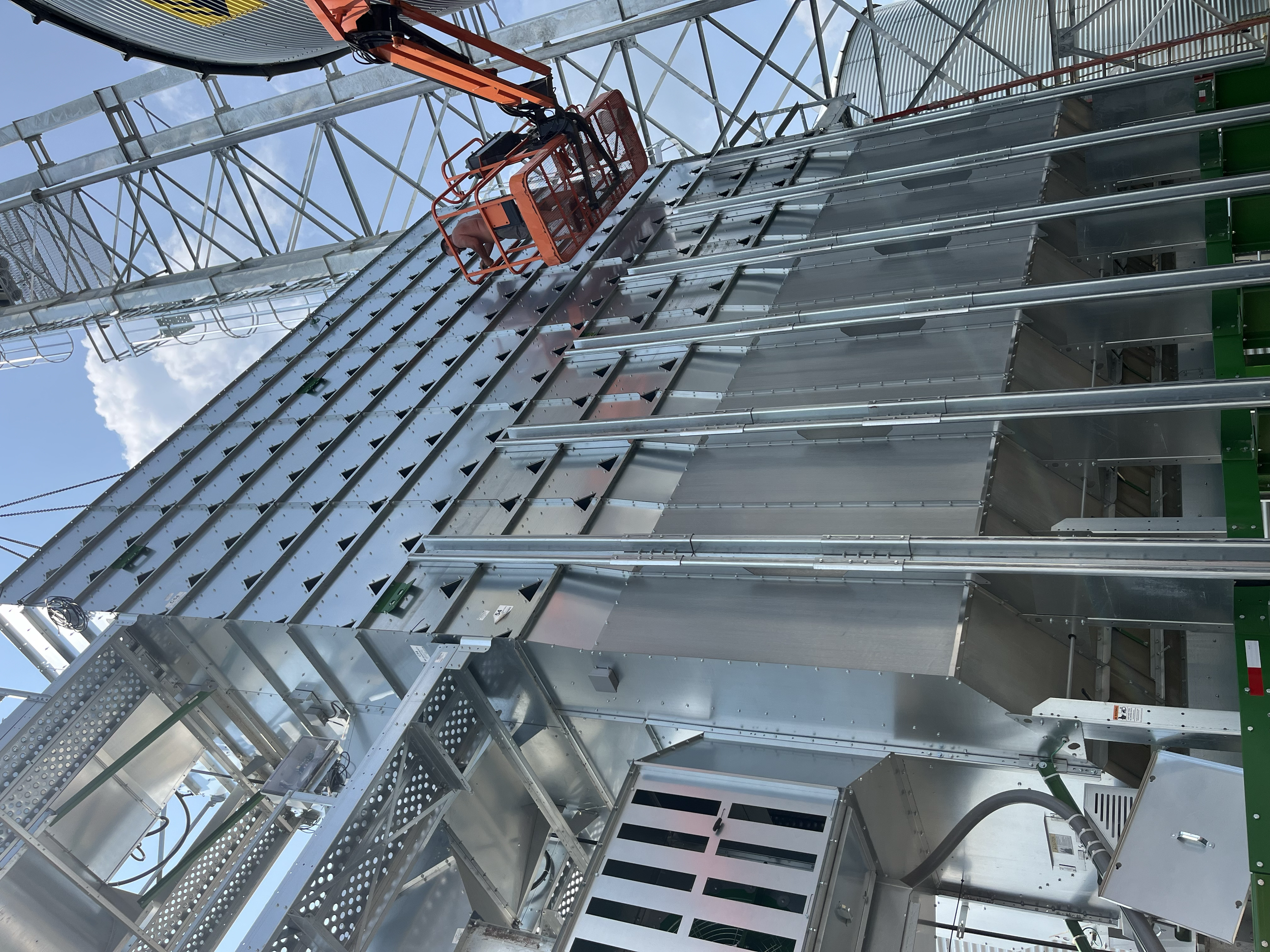 View of a worker repairing or constructing a metal roller coaster structure on a sunny day, with a clear blue sky in the background.