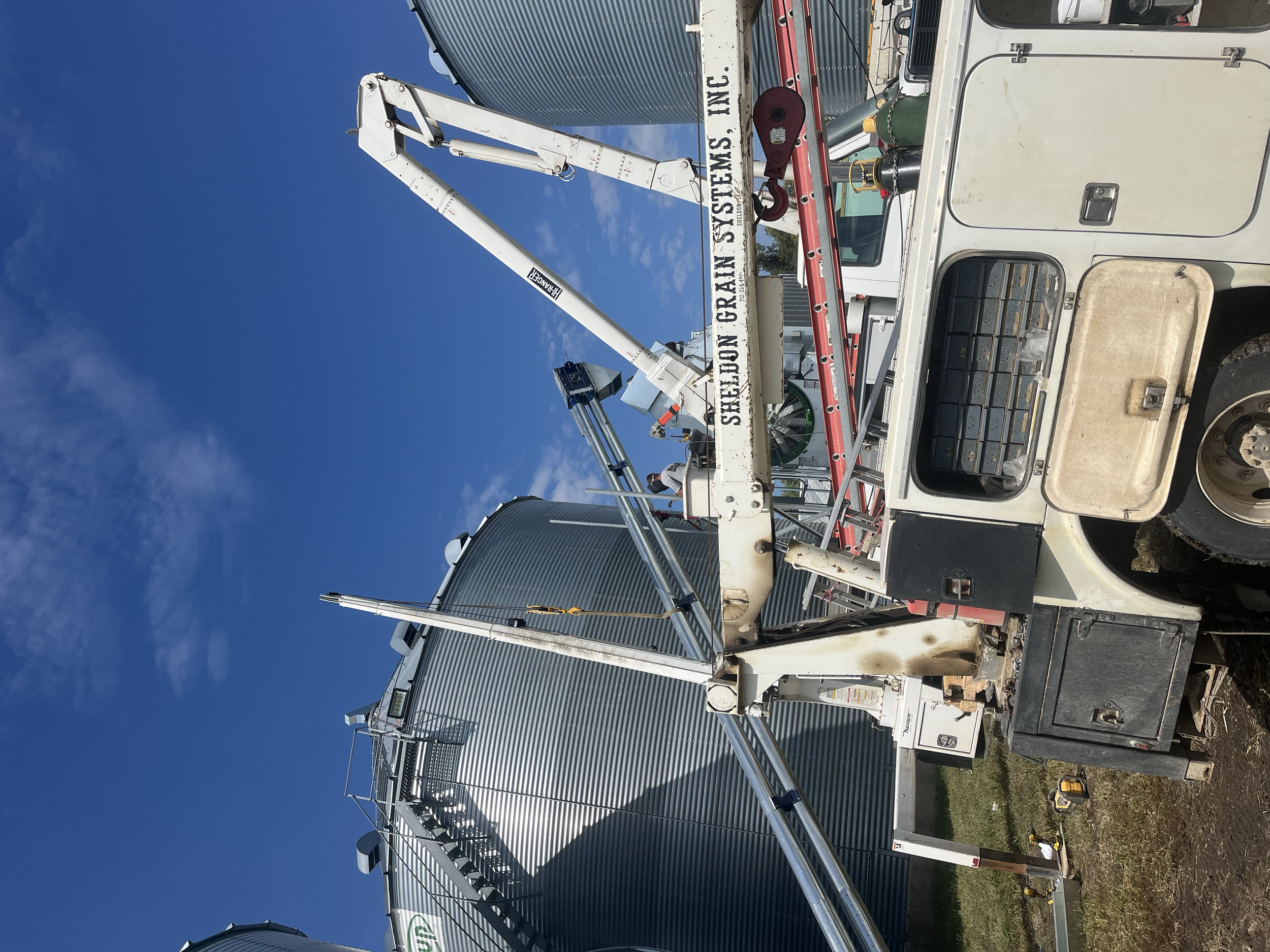 A large white utility truck with an extended bucket lift, parked outdoors under a clear blue sky. The bucket lift has a sign that reads 'Sierra Great Excavation' and 'Sierra Great Excavation Inc.' visible on the boom.
