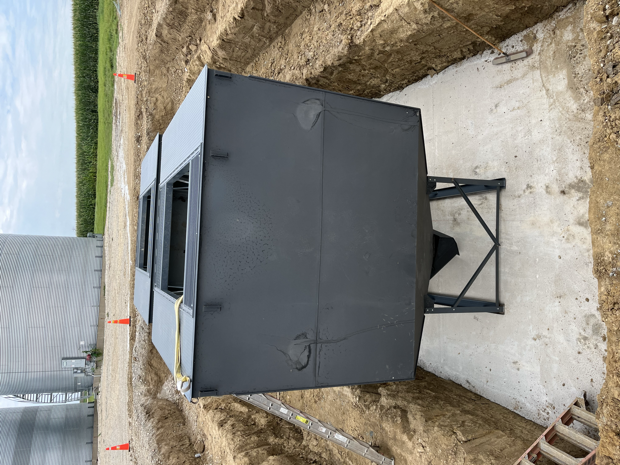 Underground utility box in a construction site with a ladder, orange safety cones, and building equipment nearby.
