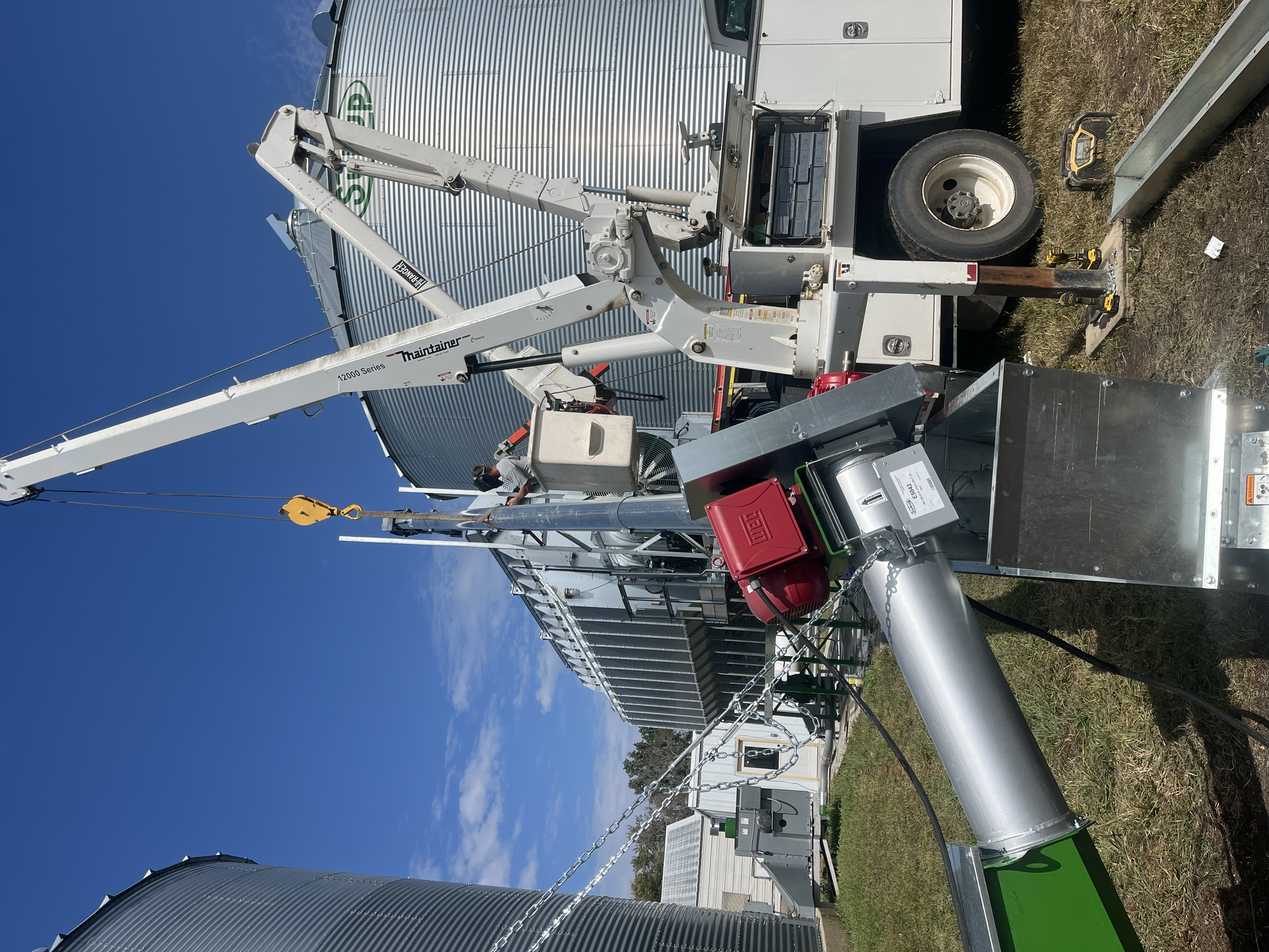 A mobile service lift with a large gray tank behind it, with some tools and equipment on the ground nearby, set outdoors under a bright blue sky.