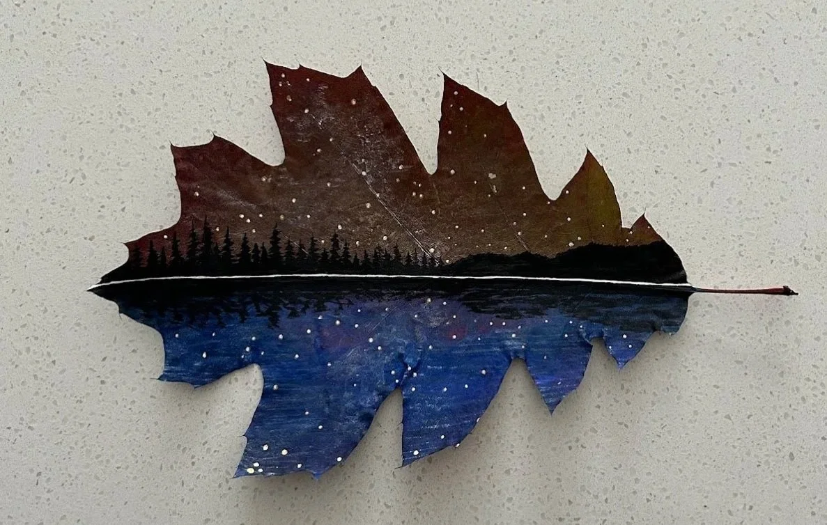 Leaf with a painted landscape of a starry night, trees, and water reflections.