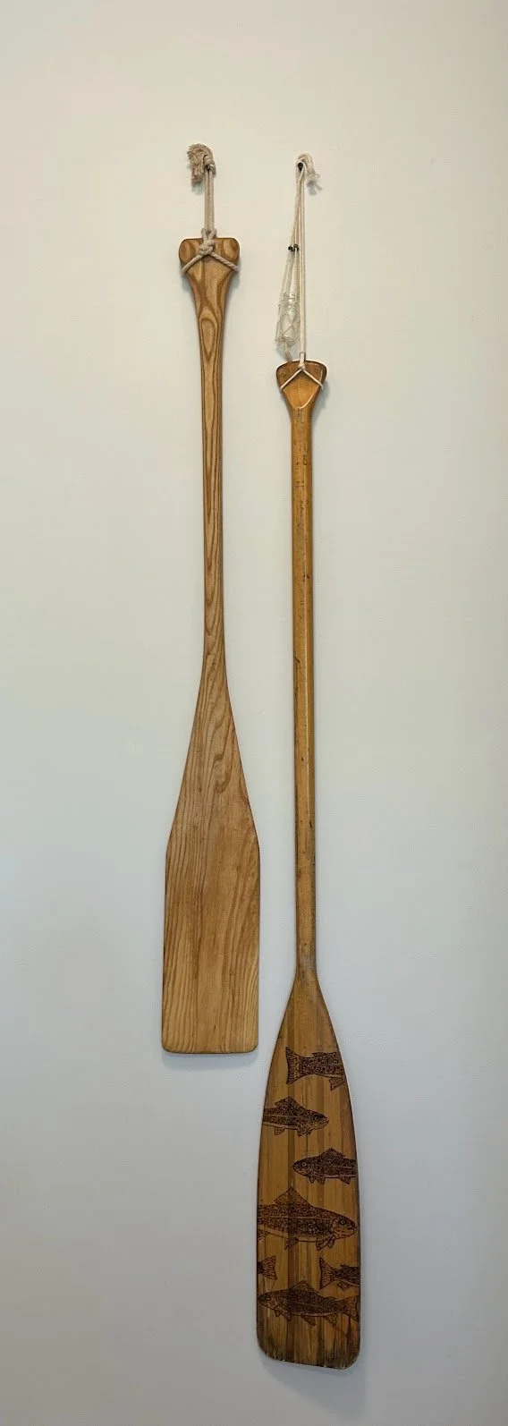 Two wooden paddles with decorative rope handles hanging on a white wall.