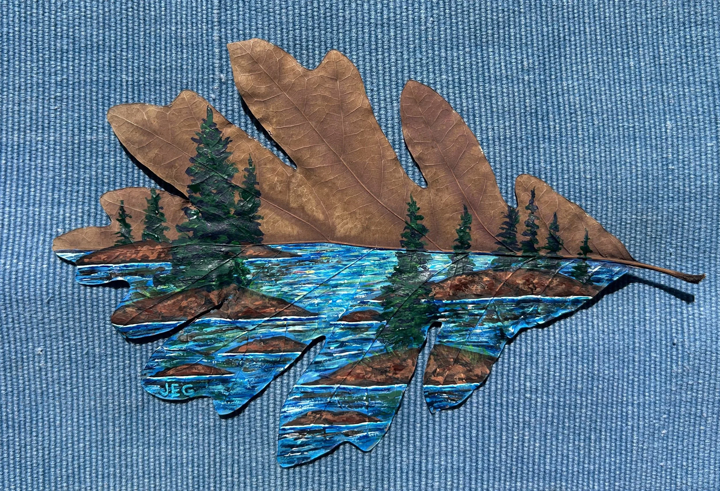 A collage of autumn leaves and painted scenery depicting a river, trees, and mountains, with a signature "JEG" at the bottom left.