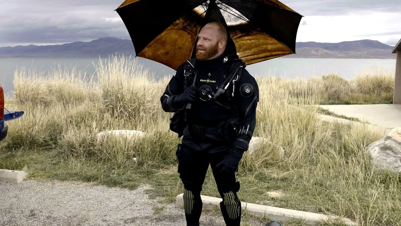 A Fathom volunteer diver on the shore of Strawberry Reservoir holding an umbrella carried out of the water, October 10, 2026