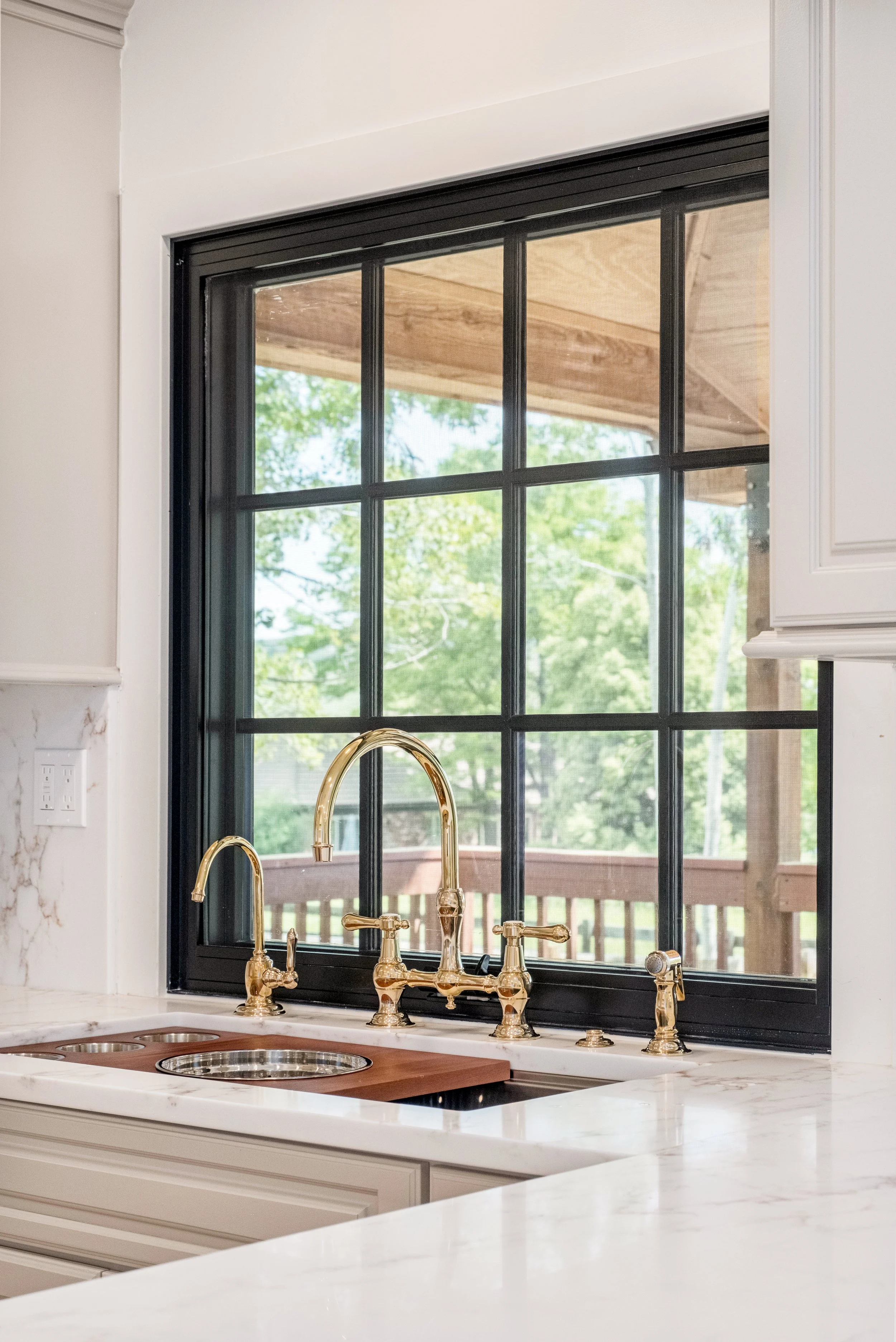 Kitchen window with black frame above a white marble countertop and gold faucet.