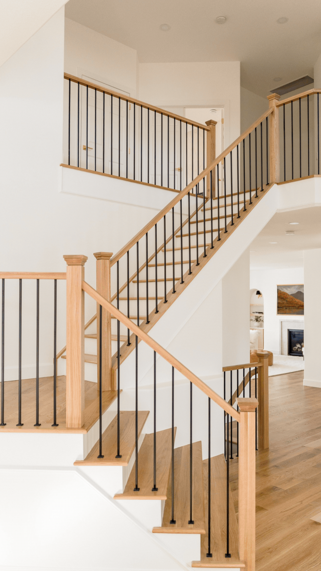View of a staircase with wooden handrails and black metal balusters in a bright, modern home interior.