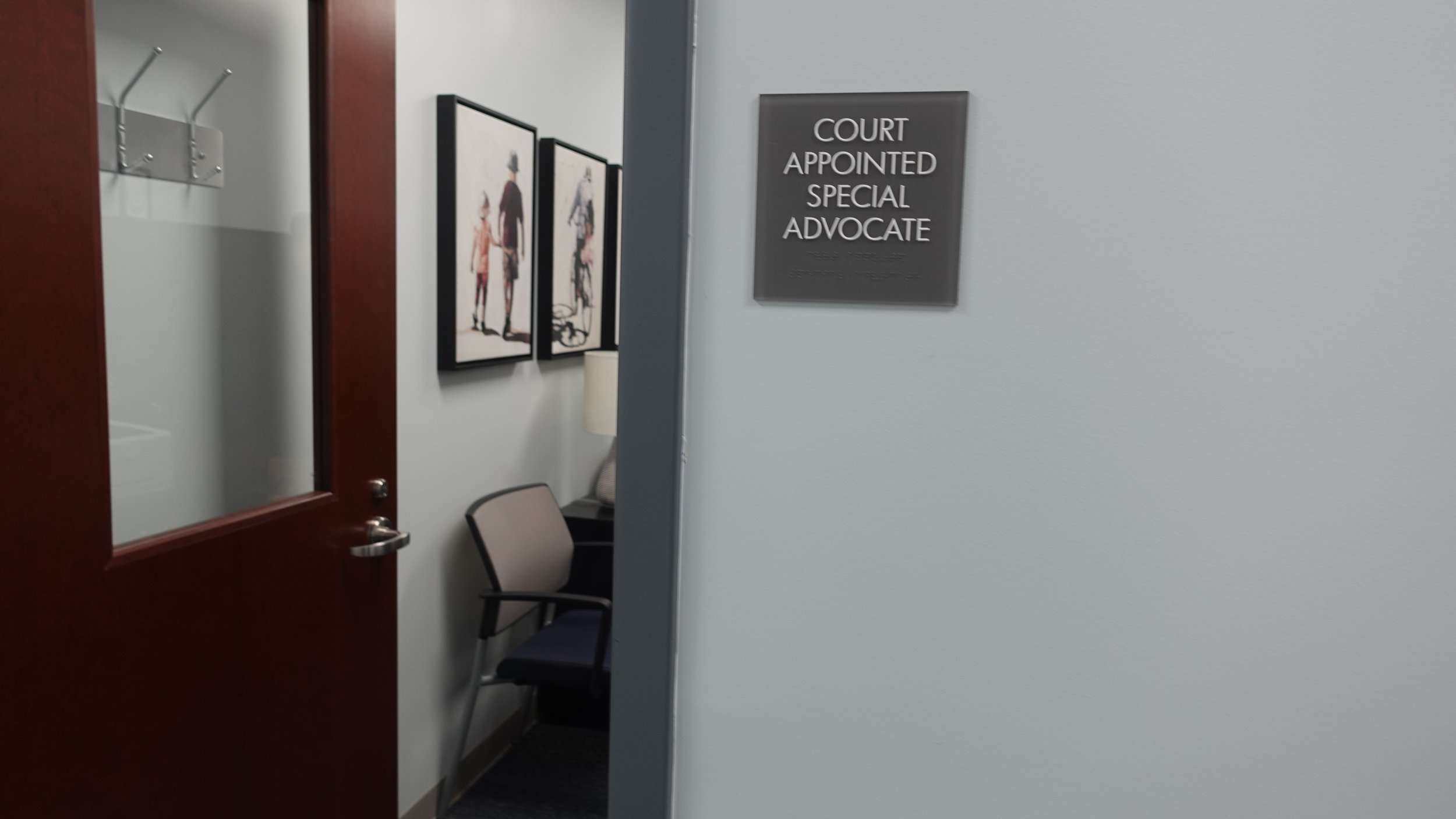 Interior view of the Warren County Common Please Court, with a sign reading 'Court Appointed Special Advocate' on the wall, a chair, and framed artwork of children and adults.