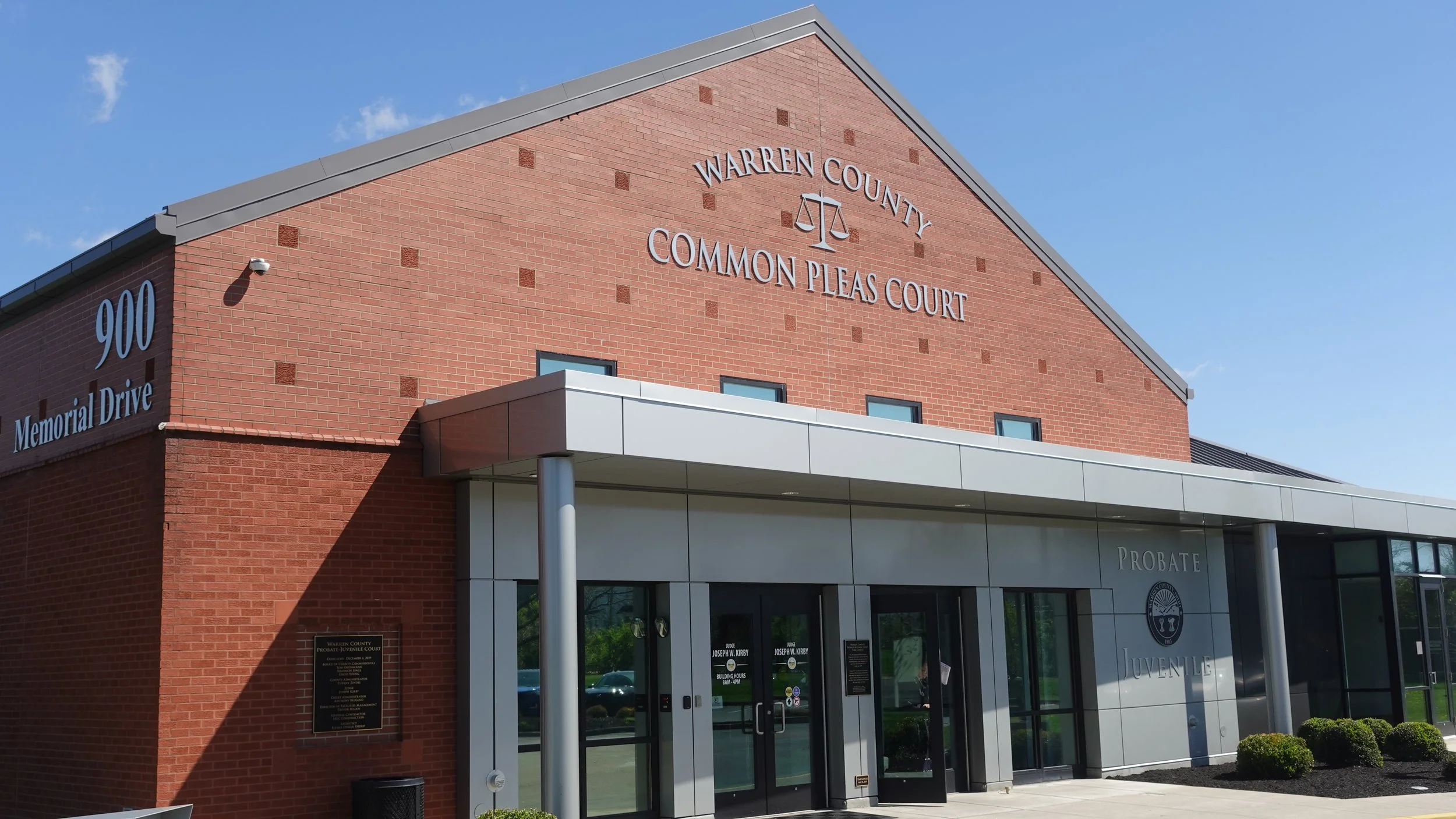 Exterior view of Warren County Common Pleas Court building, made of red brick, with the courthouse name and scale symbol on the upper facade, and a modern entrance with glass doors and metal framing.