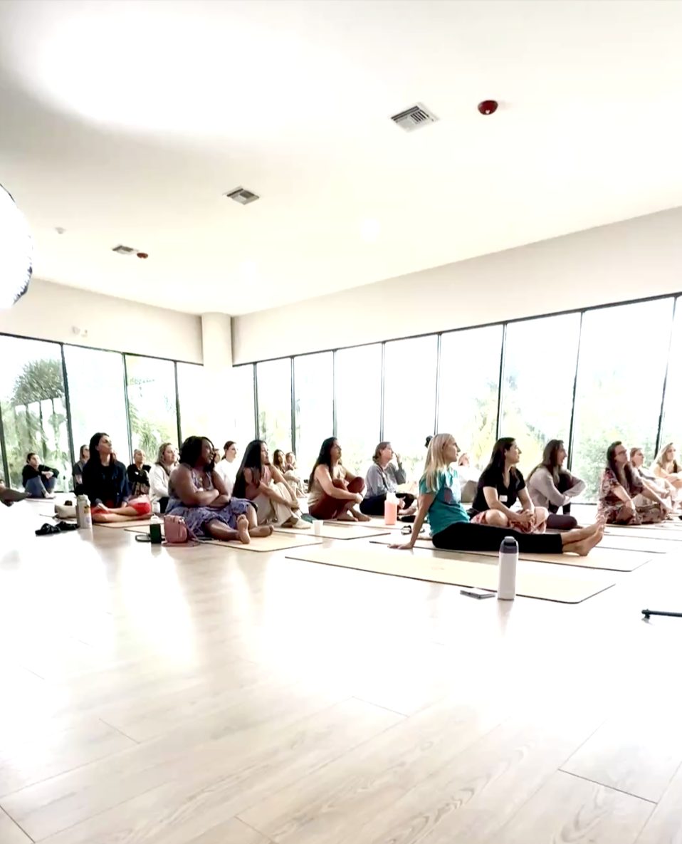 Women participating in a yoga class in a bright studio with large windows.