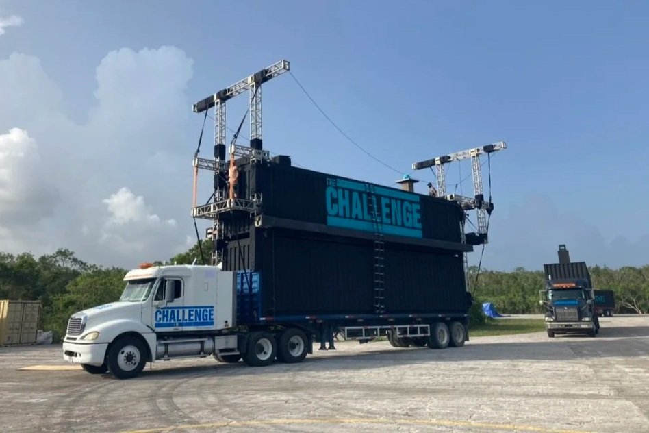 Truck with a mobile stage labeled 'The Challenge,' set up outdoors on a paved area with trees in the background.