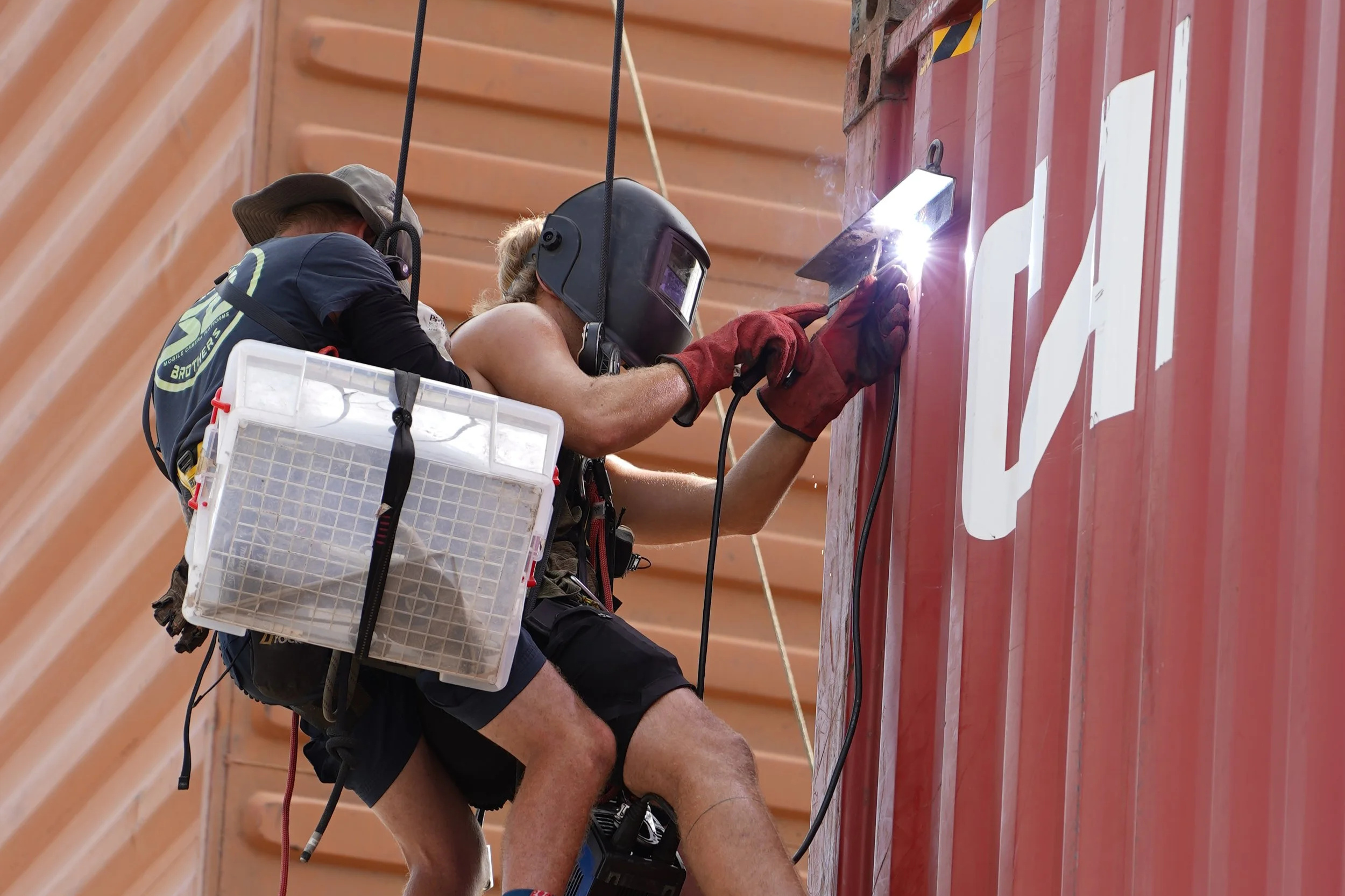 A construction worker welding on a red wall while wearing a protective helmet and gloves.