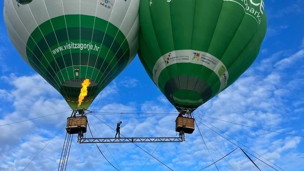 Two hot air balloons in the sky, one with a flame, and a person walking on a platform between them.