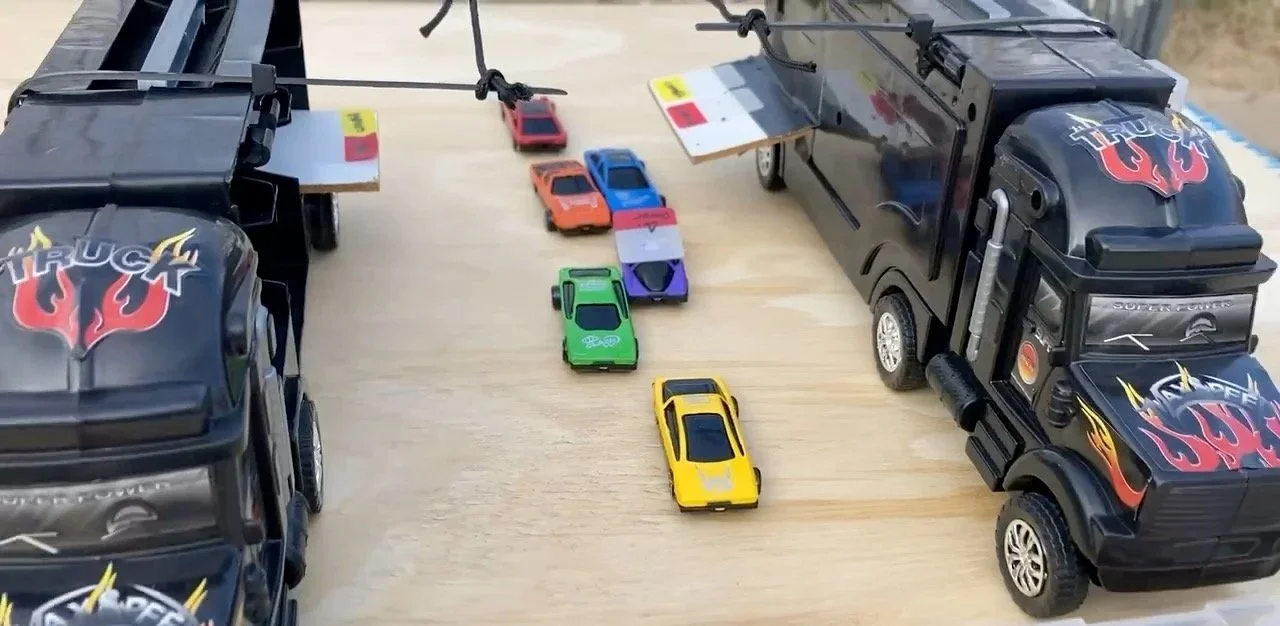 Toy cars arranged in a line between two toy trucks on a wooden surface.