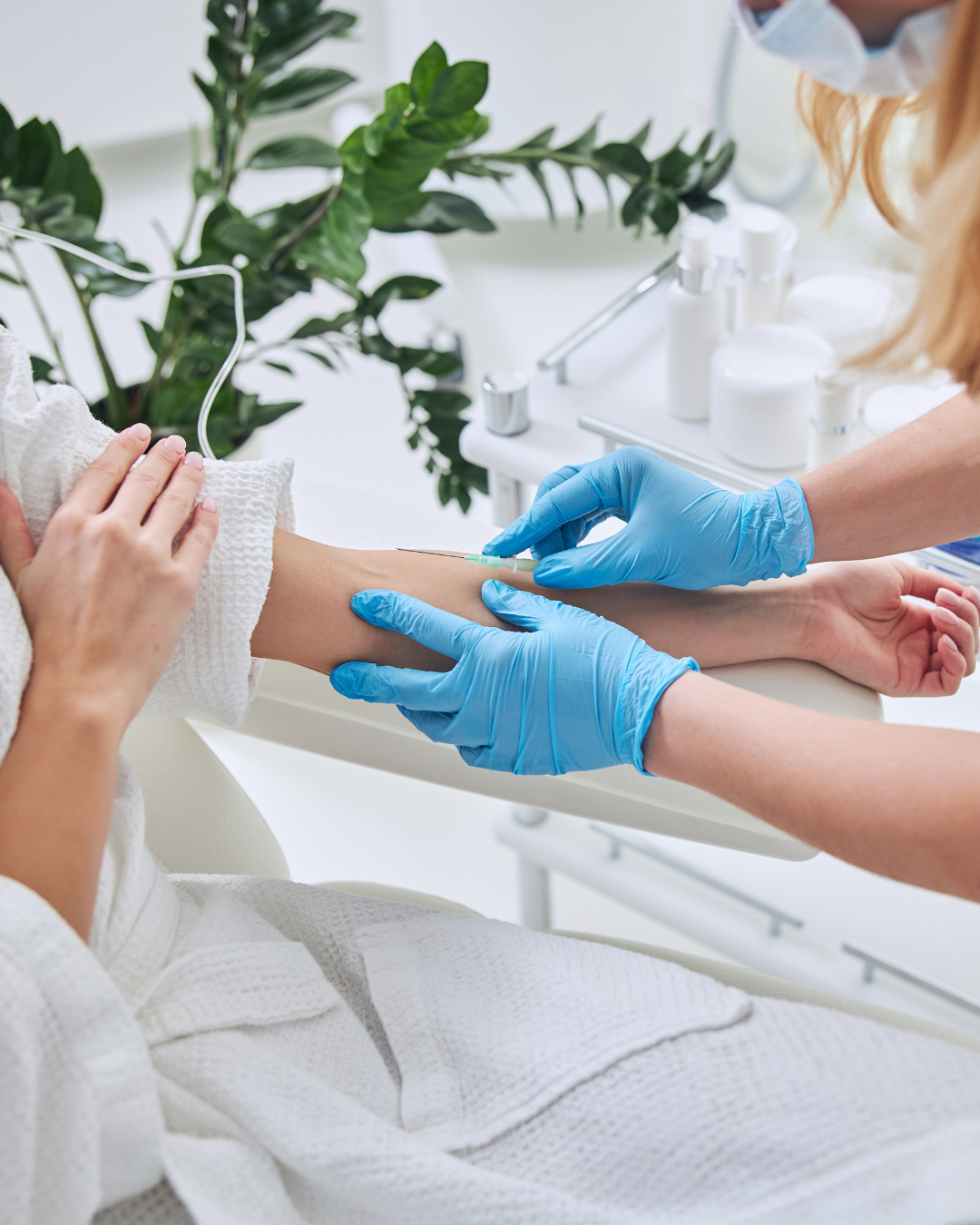 Healthcare professional with blue gloves giving an injection to a patient's arm during a medical procedure in a bright clinical setting.