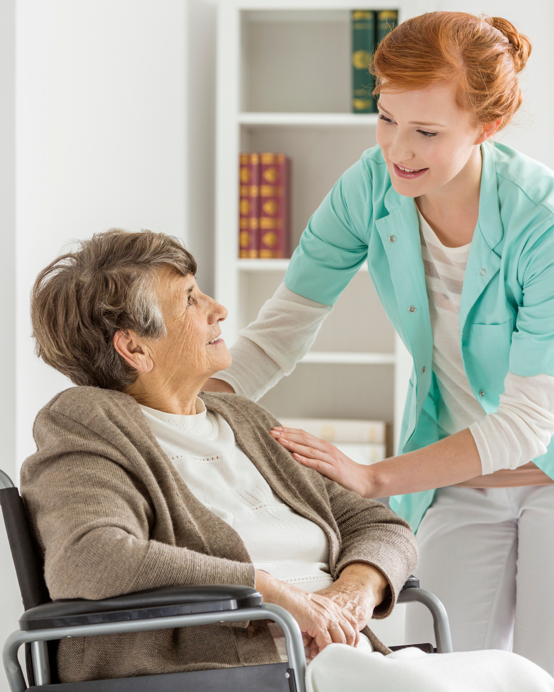 A nurse caring for an elderly woman in a wheelchair, smiling and making eye contact in a medical office.