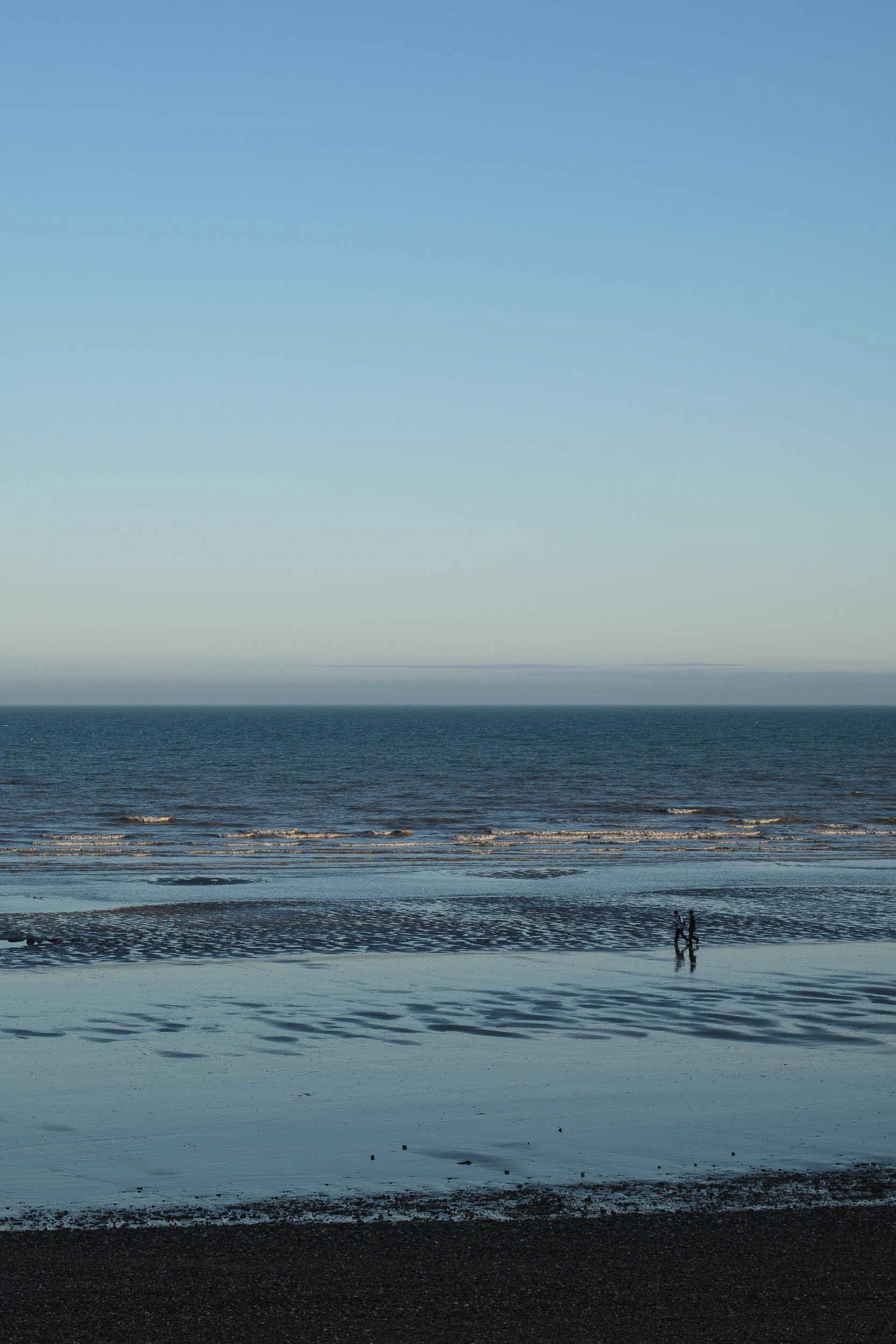 Abstract colour scene of two people walking on the beach at low tide where the blue colours reflect the sky like a mirror