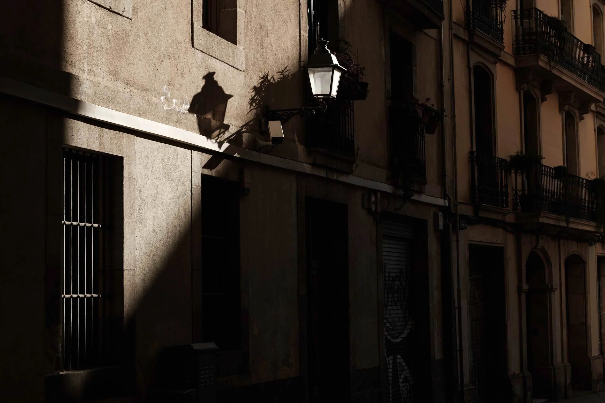 Golden hour view of a an old building's facade with multiple windows and balconies, illuminated streetlamp by the sun with shadows on the wall in a minimal fashion.