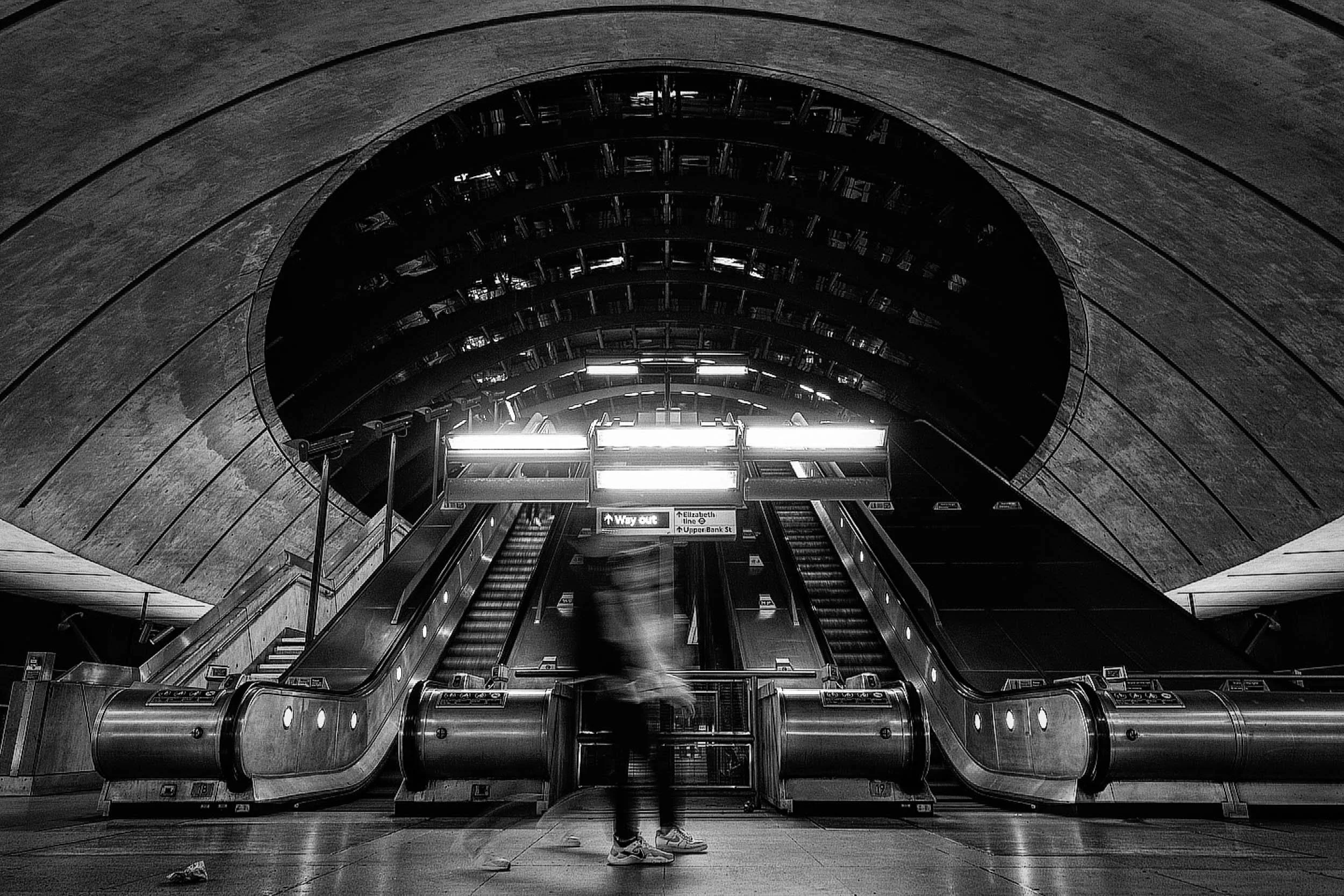Canary Wharf Underground Station in Black and white wide angle motion blur showing enormous dome like architecture with glowing lights