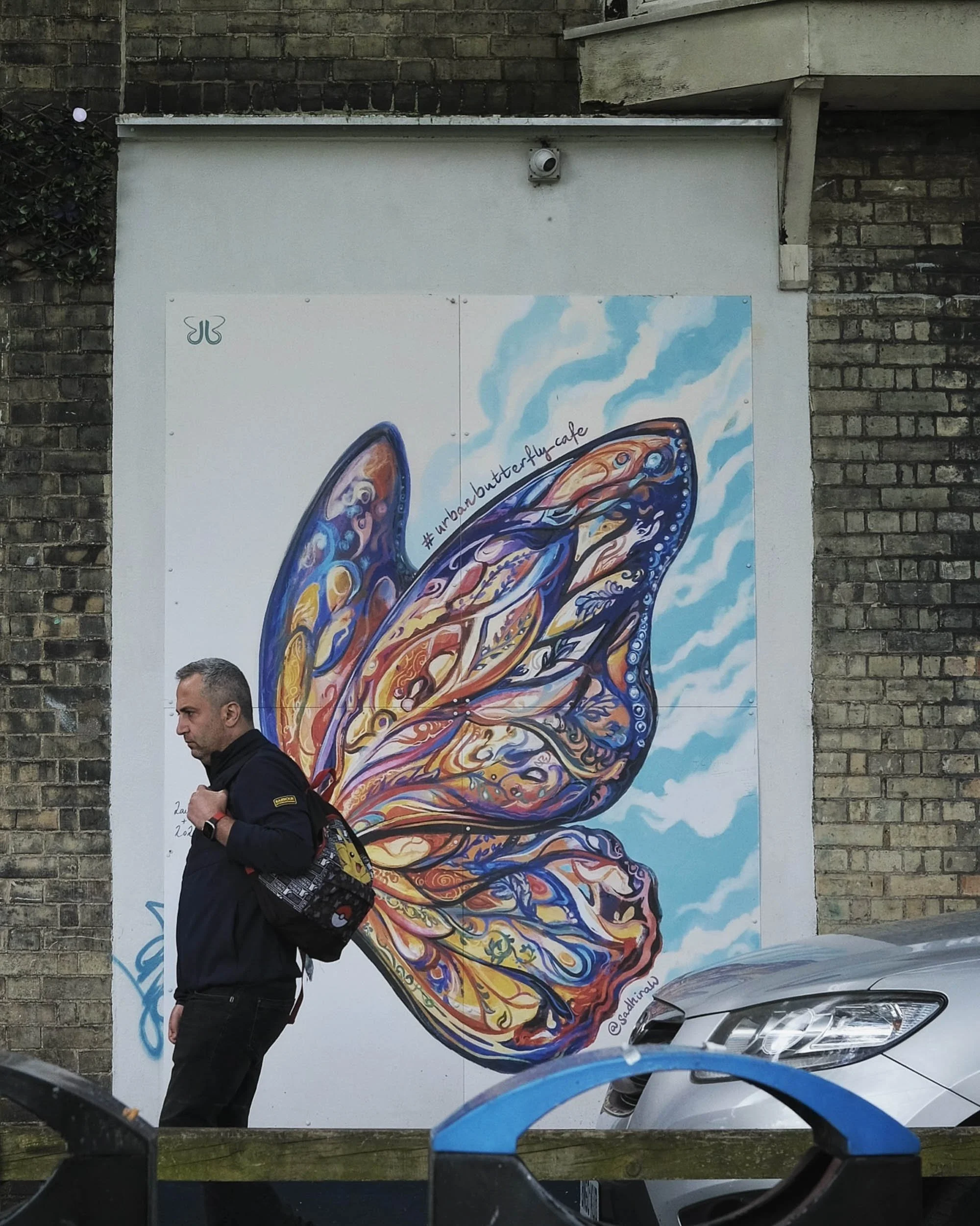 Street scene of perfectly timed shot as a man passed by a grafiti mural of a butterfly creating the illusion that the man has wings as a surreal painting