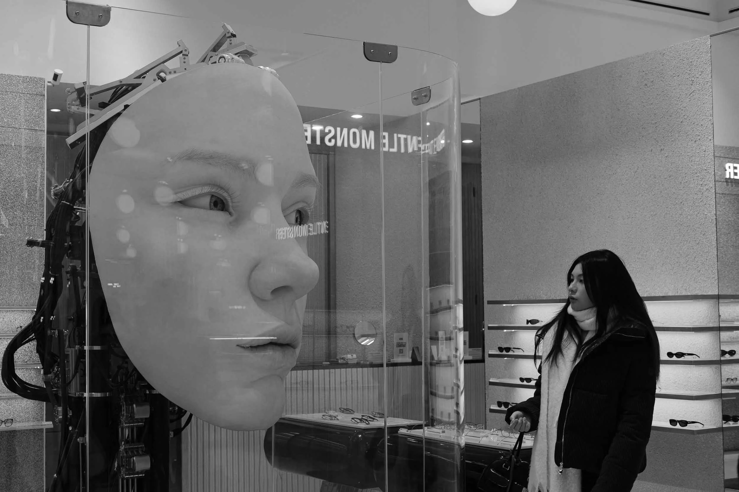 Black and white scene a woman looks at a giant robotic human face that looks suspiciously at her in London