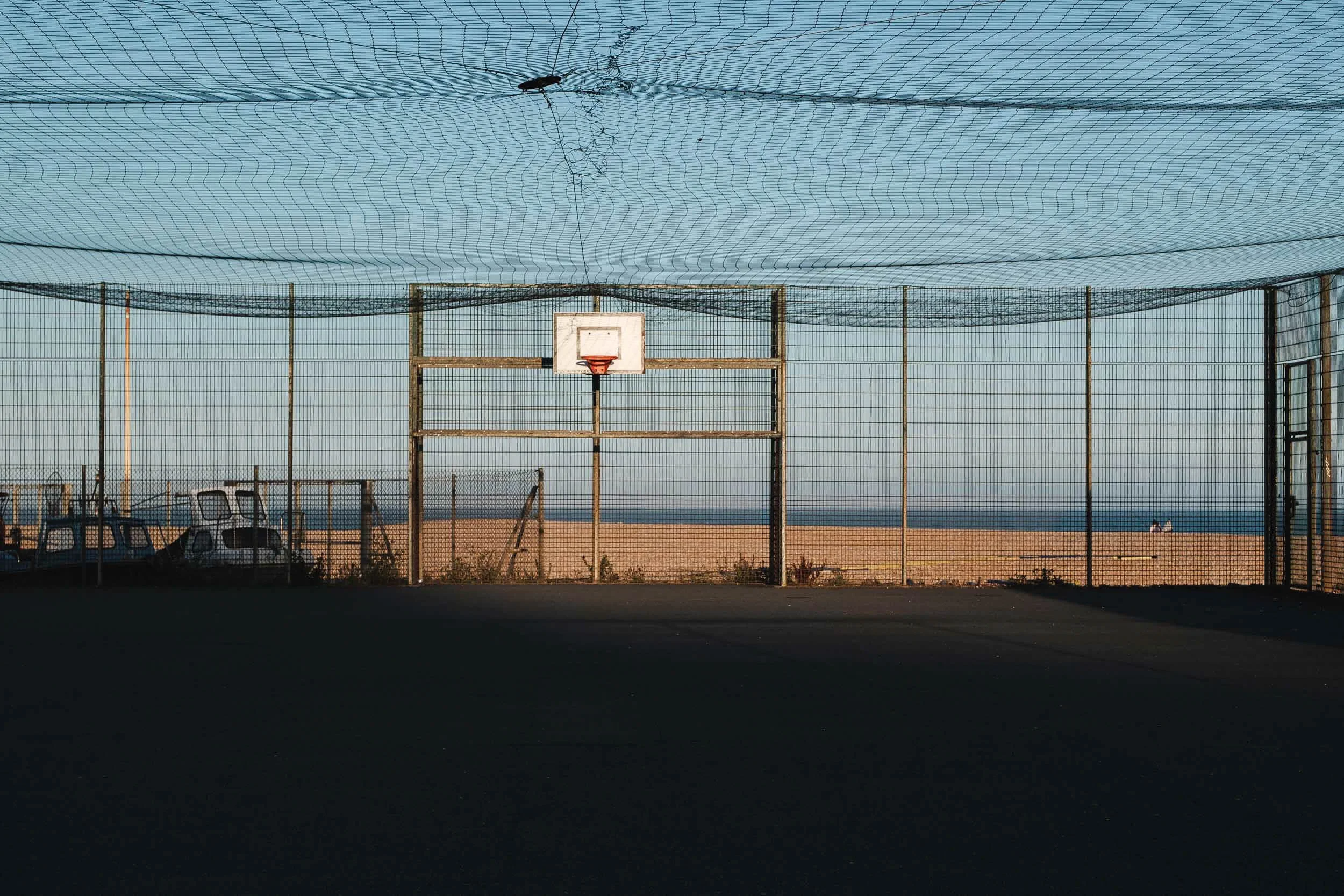 Golden hour creates long shadows on a basket ball court with a view to the beach