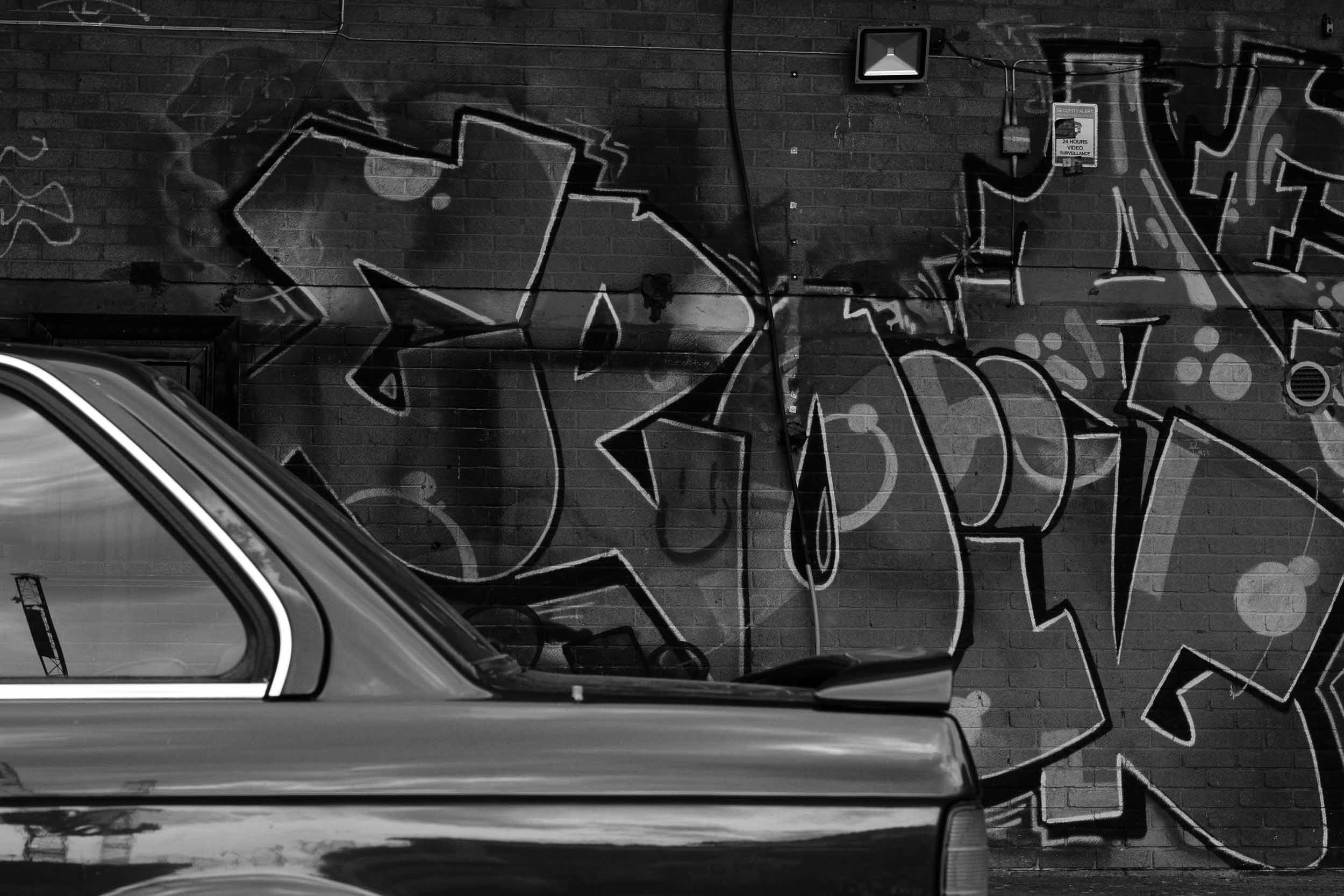 Black and white graffiti with car parked infront reflects light in on an London industrial estate
