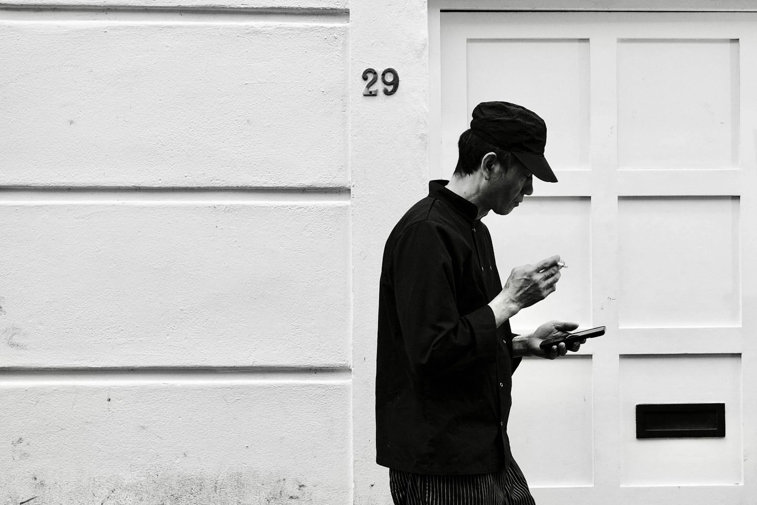 High contrast black and white image of a man having a quiet moment and cigarette in Chinatown London framed by the door to no 29