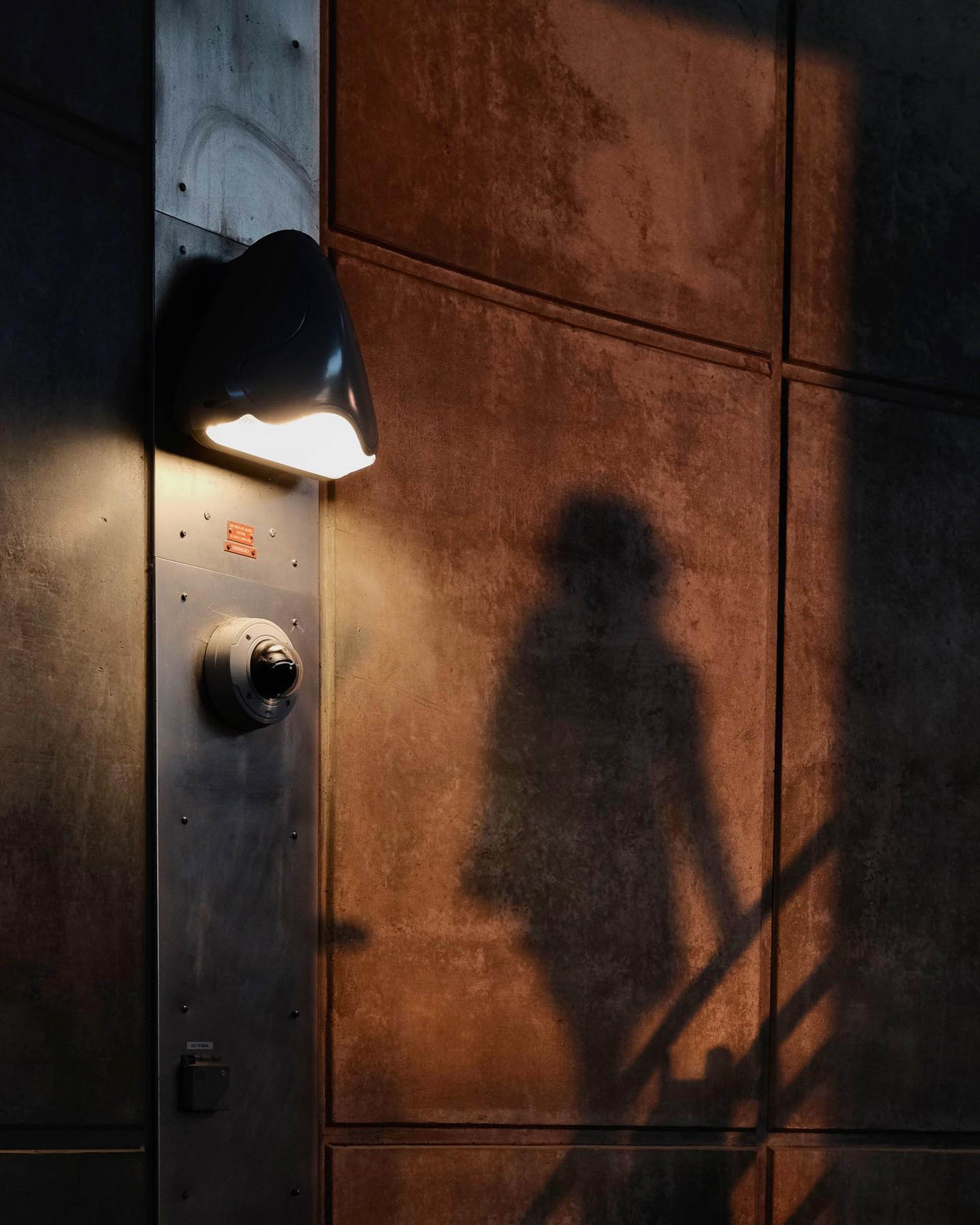 The silhouette of a woman walking on the brutalist concrete architecture of a London Underground station illuminated by warm orange sunset and neon glow