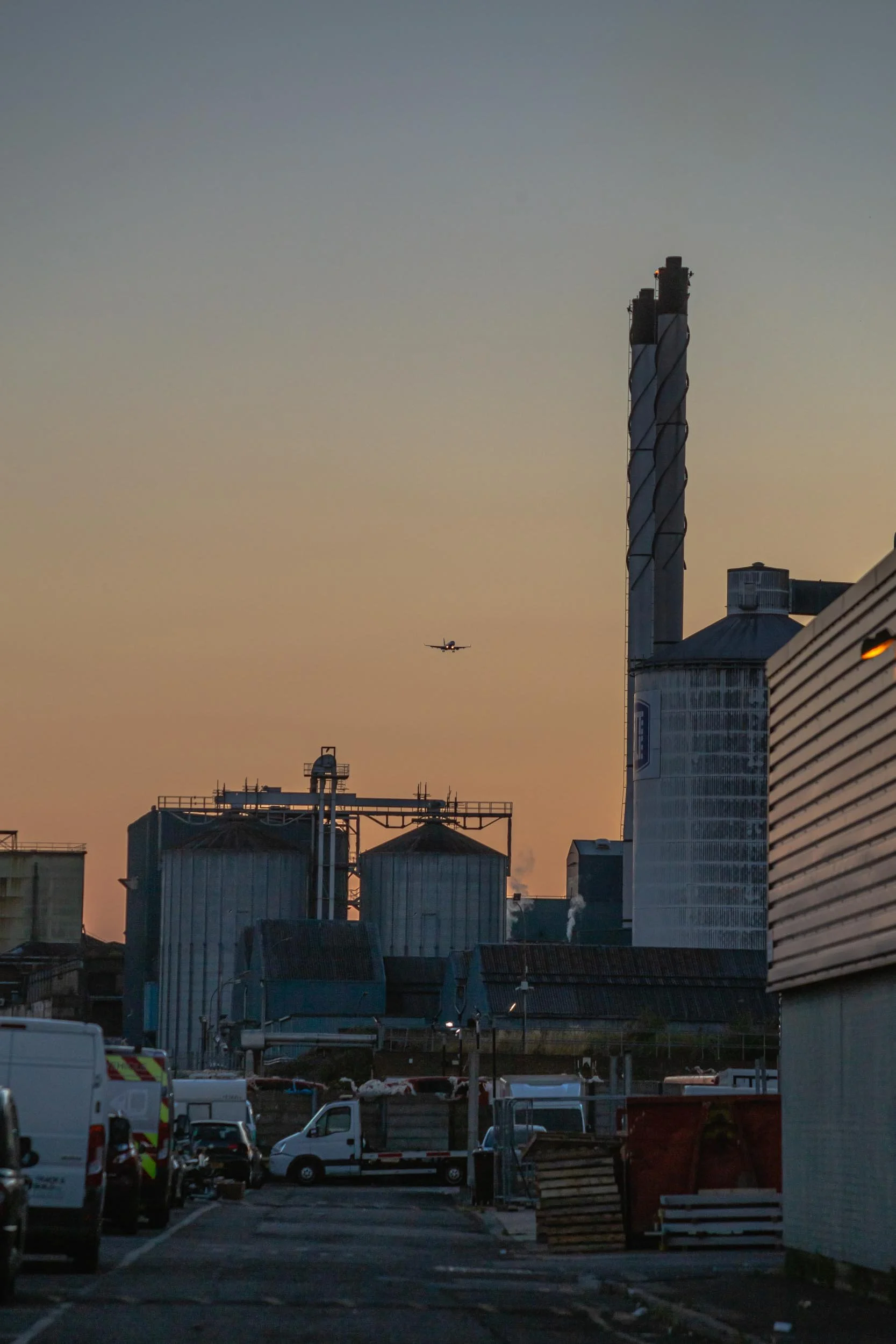 A plane comes into land at London City Airport, viewed from an industrial estate near the Tate & Lyle sugar factory, East London Royal Docks, E16. Golden Hour..