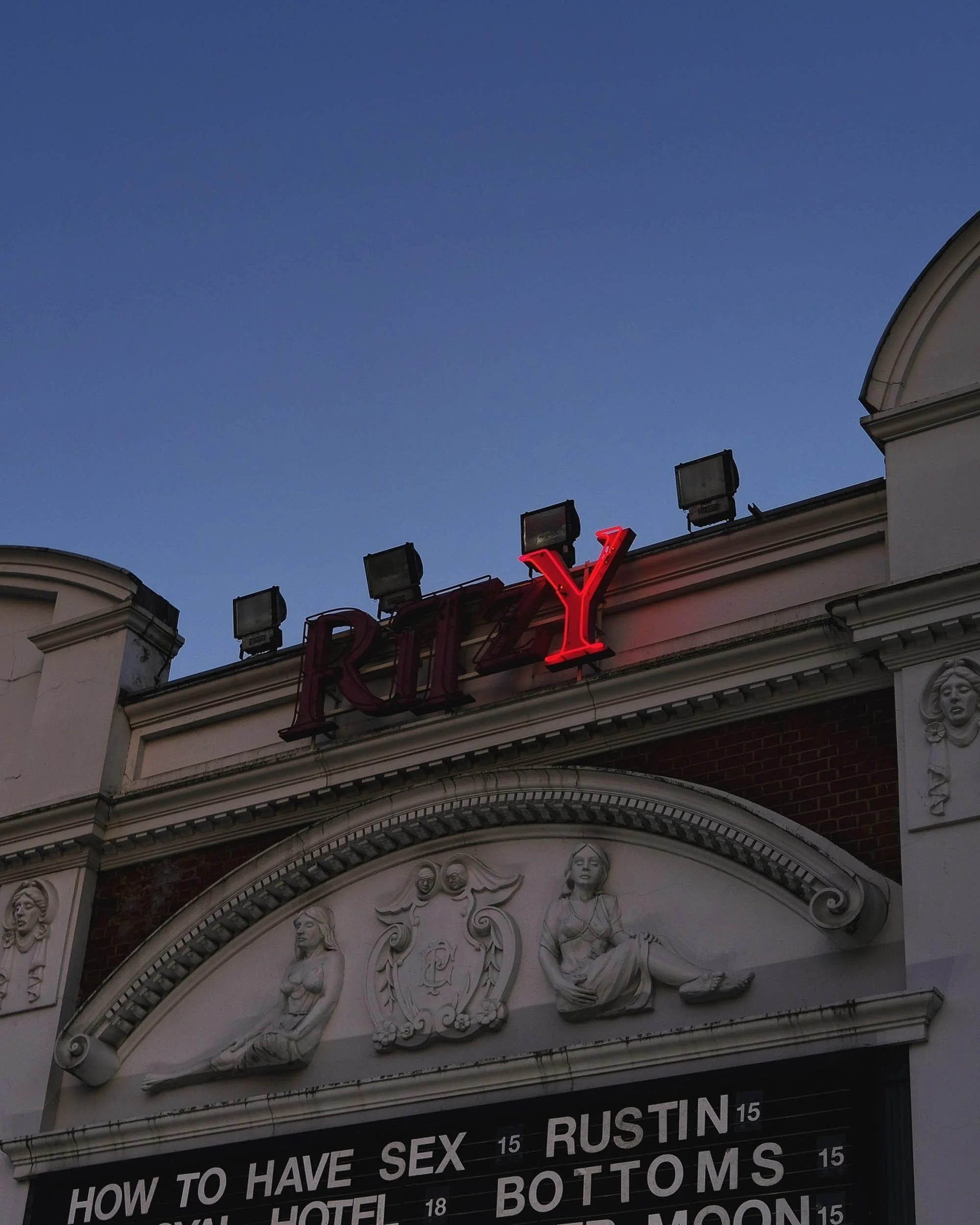 Red neon sight set againts a blue hued evening sky in Brixton South London the Ritzy Cinema shows films on with half illuminated Ritzy neon sign