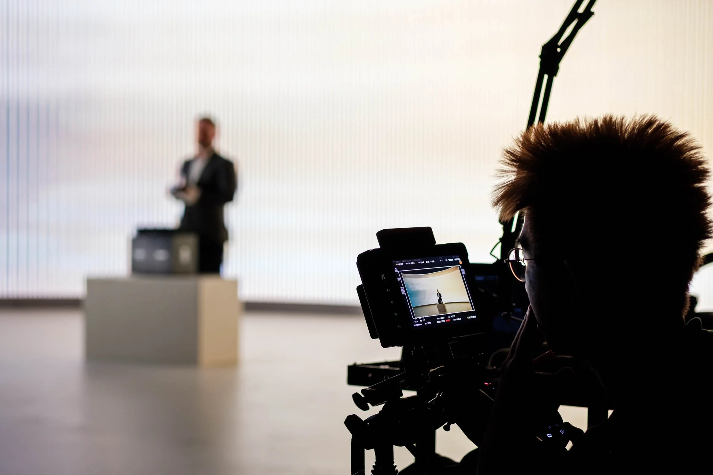 shallow depth of field shot with a camera operator checking a small monitor with a man standing in the distance holding a product in front of large LED screen