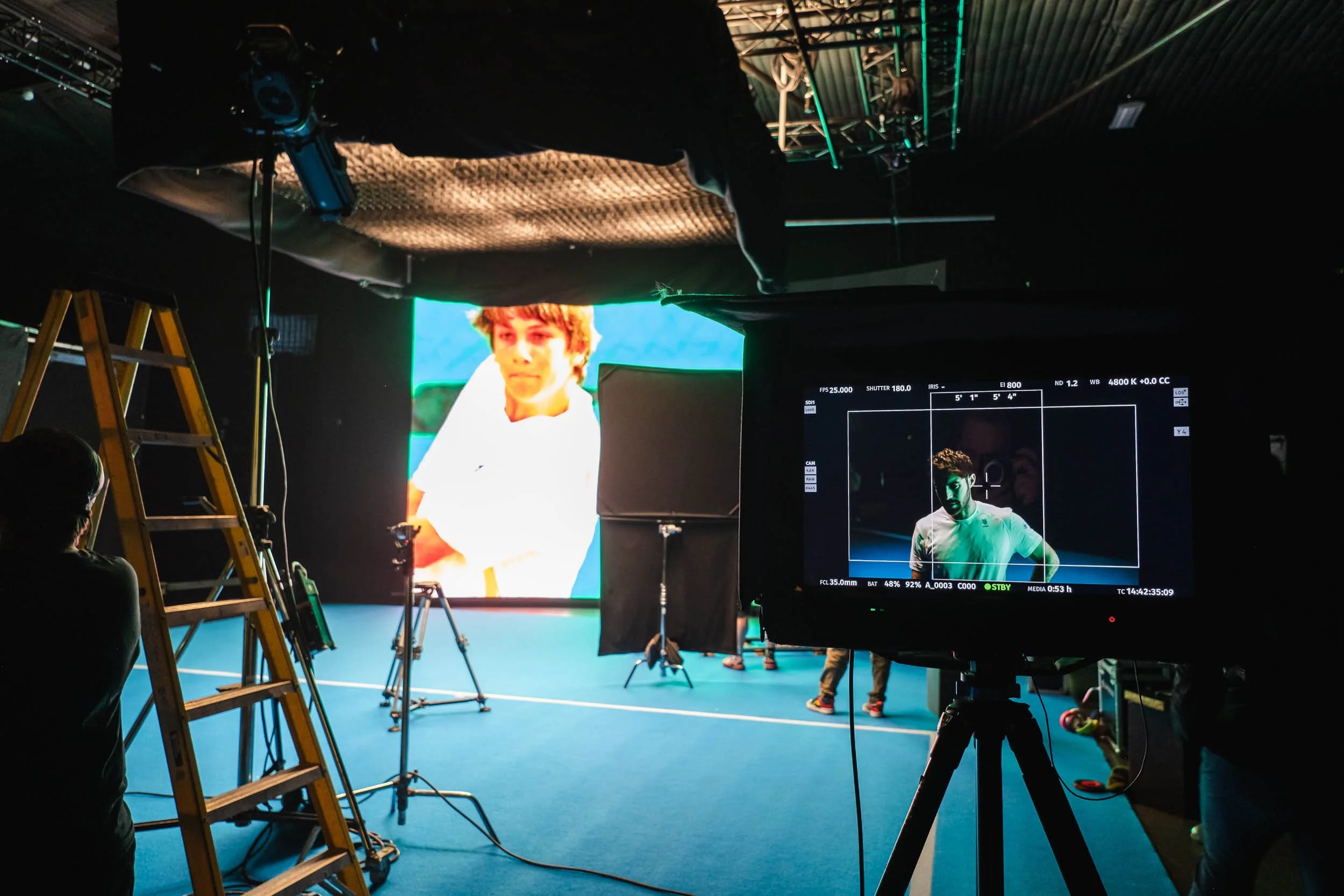 Behind the scenes shot at a shoot for a brand featuring a professional male tennis player and a large LED screen and various photographic and filming equipment