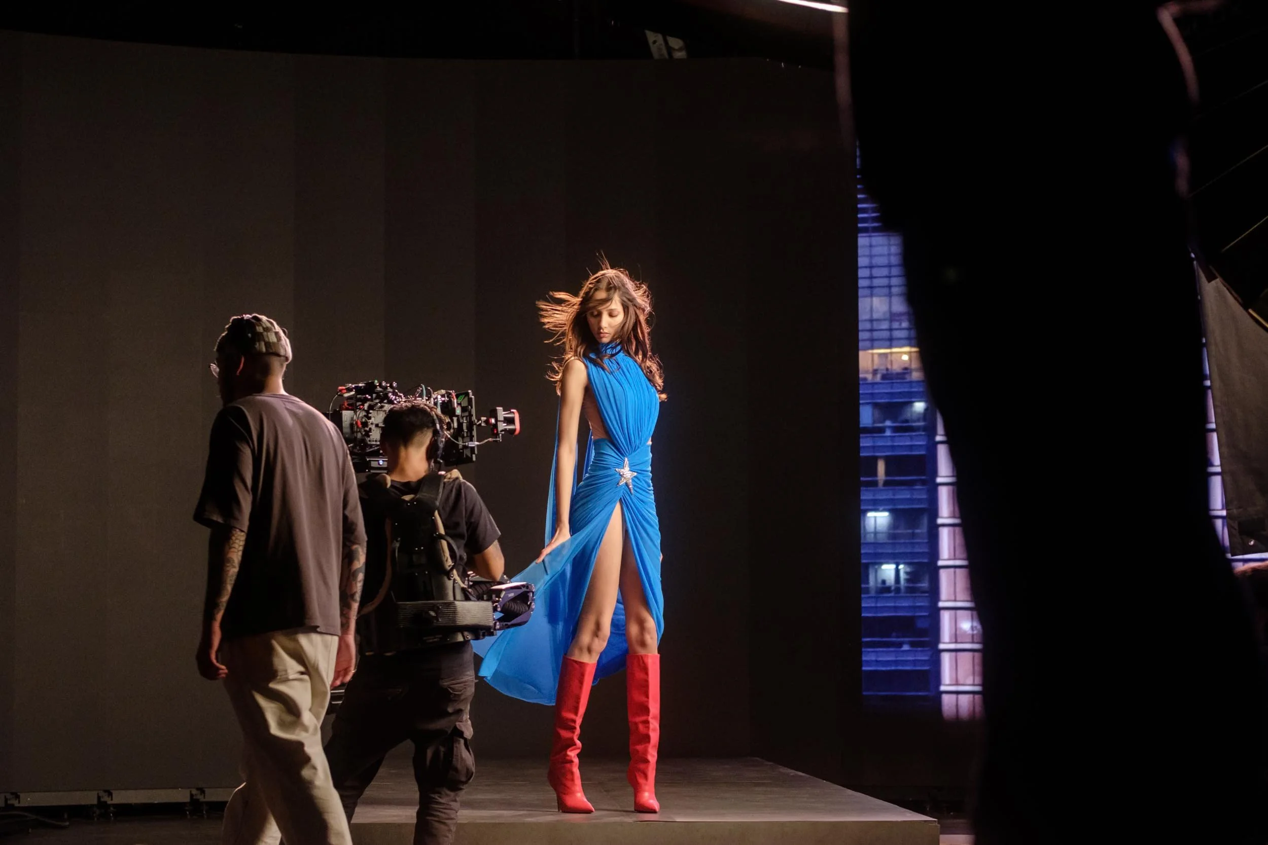 Female model strikes a pose at a fashion shoot in a striking blue dress with high red boots in the new David Koma Super Girl line launch