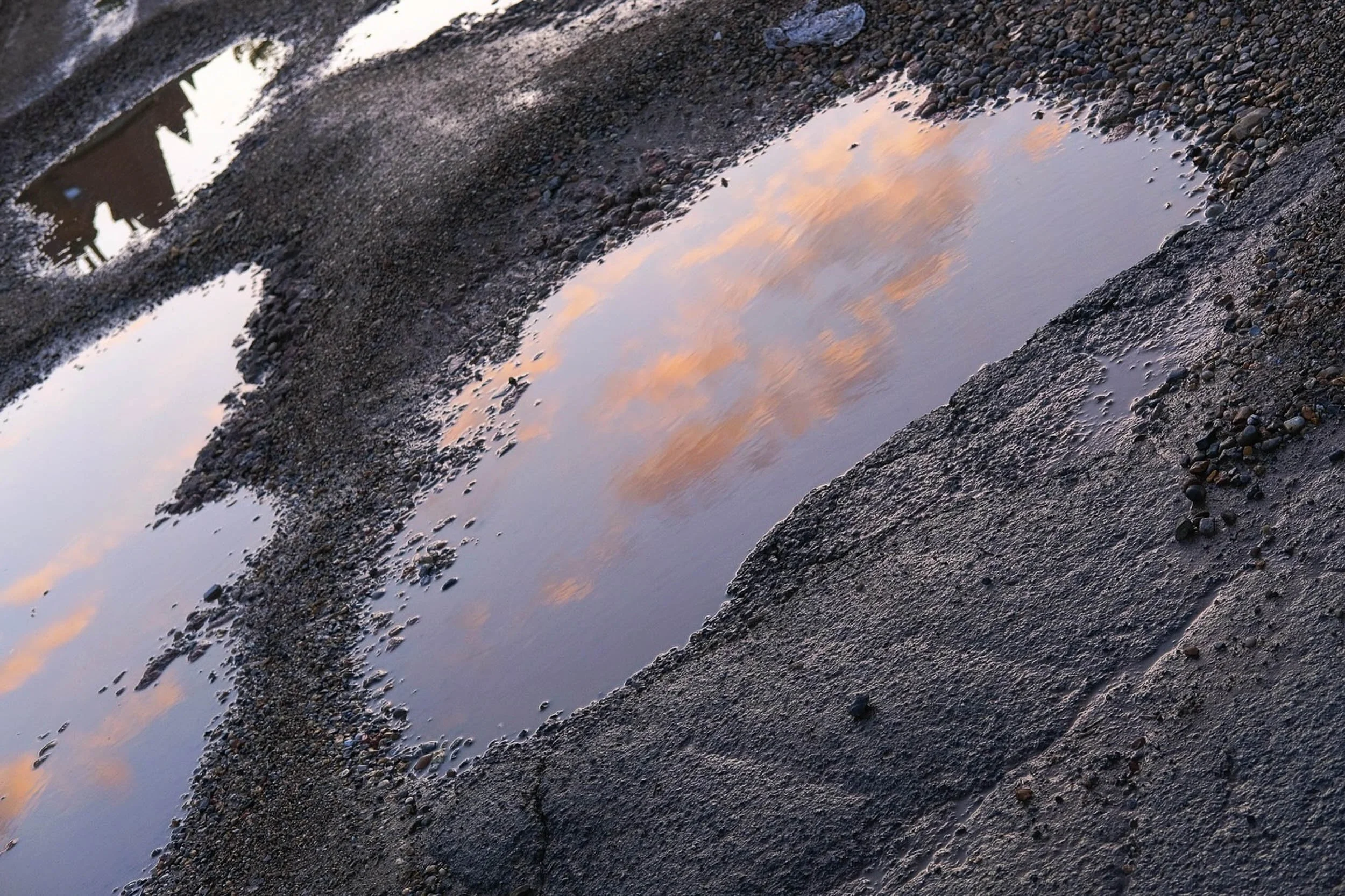 Abstract colour image of pink clouds on blue sky at sunset golden hour within a puddle reflection on the ground in Chingford London