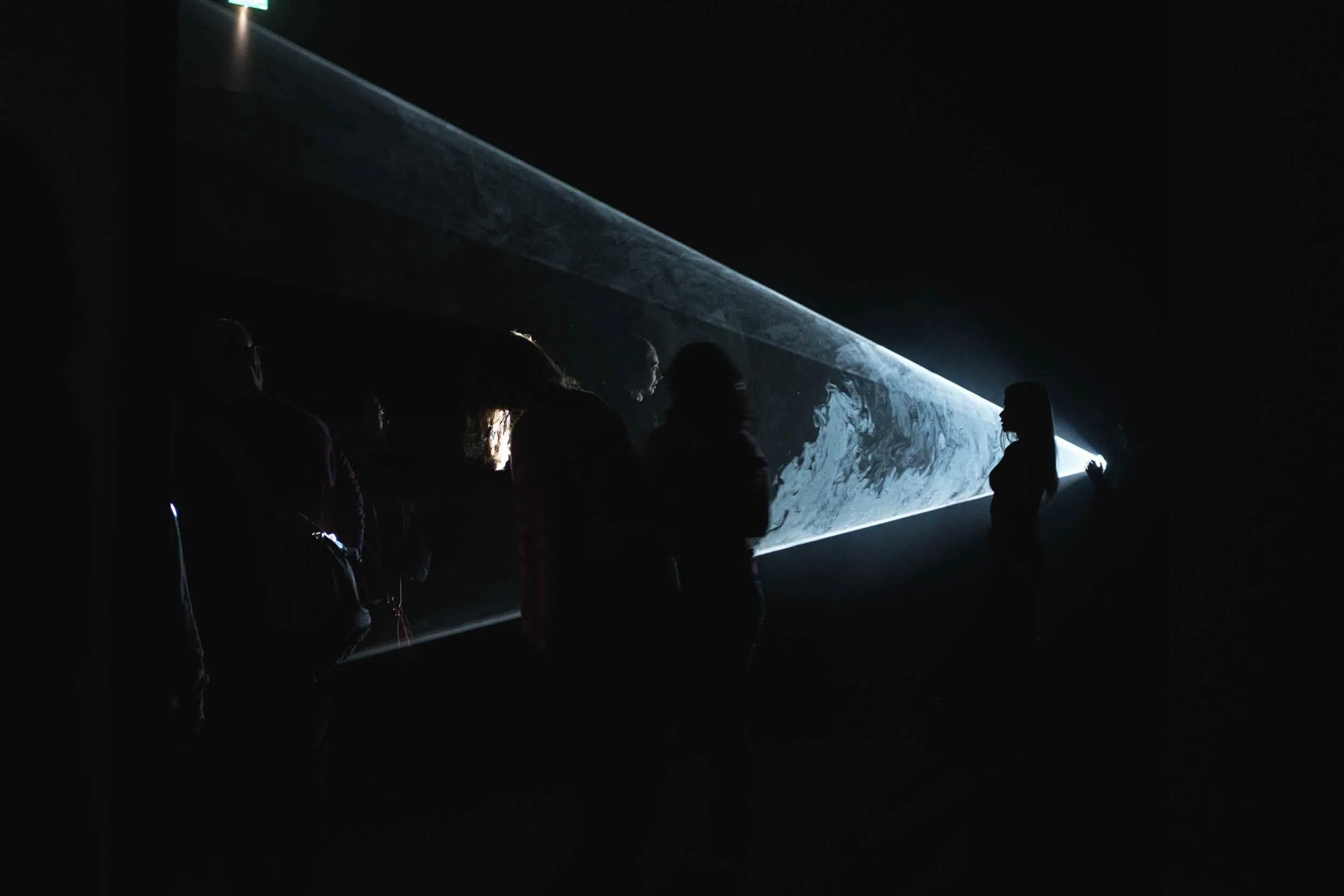 People interacting with light beams at an art installation at the Tate Modern in London, in a dark room the beam of light creates silhouettes of the people.