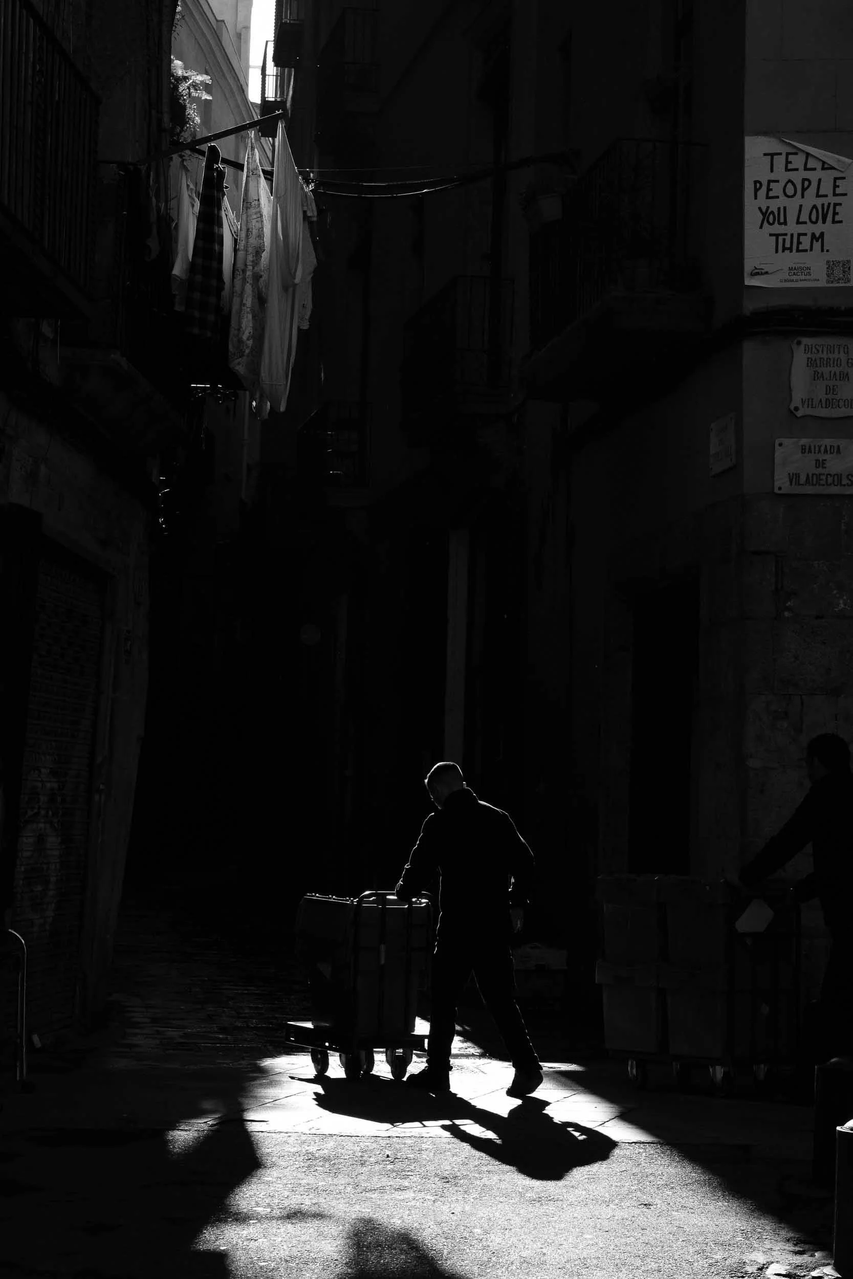High contrast black and white scene in Barcelona's Gothic Quarter a man pushes a trolley through a pool of light creating a powerful backlit scene with incredible shadows