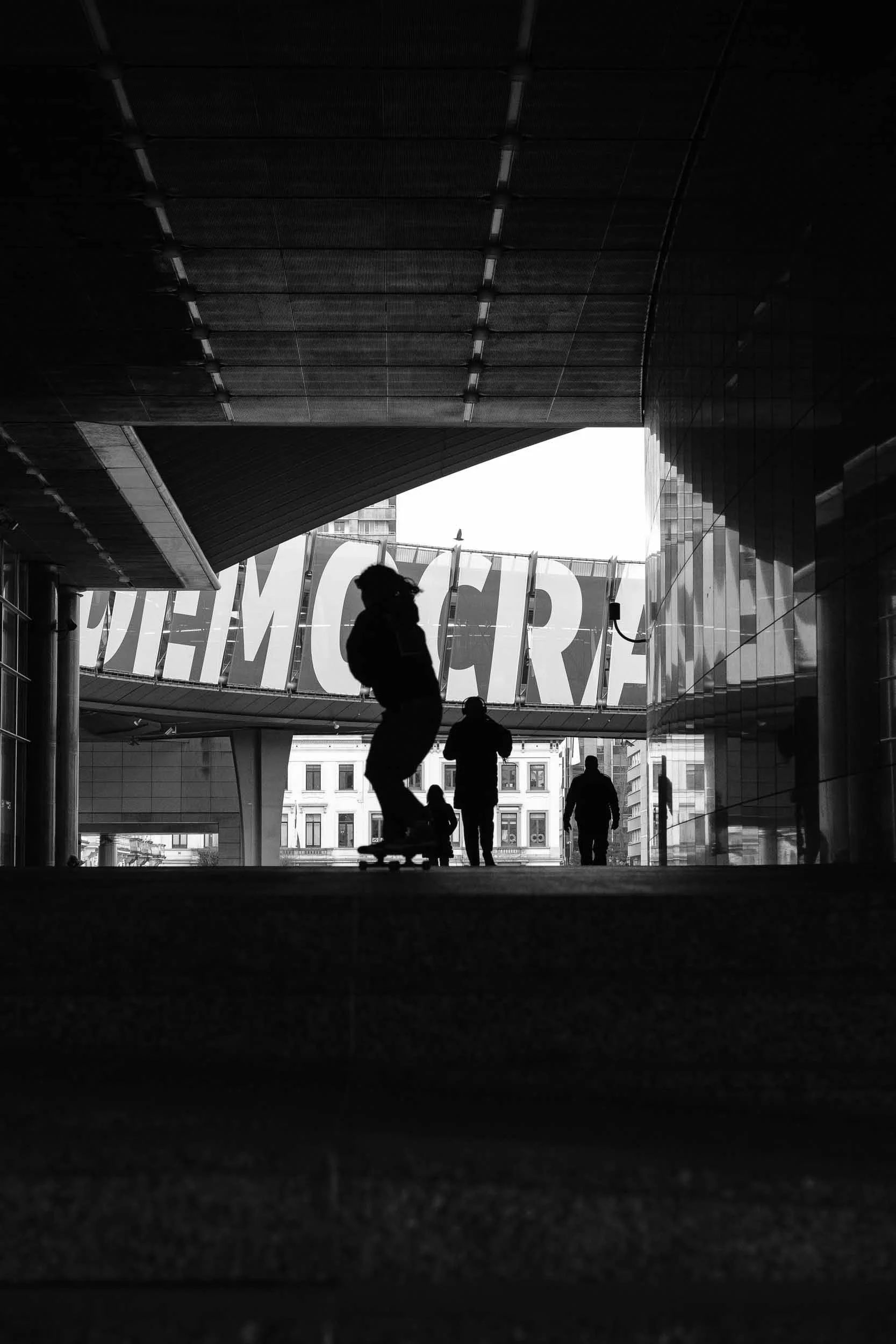 Black and white high contrast scene as a silhouette of a skater in front of a giant sign that reads Democracy in Brussels