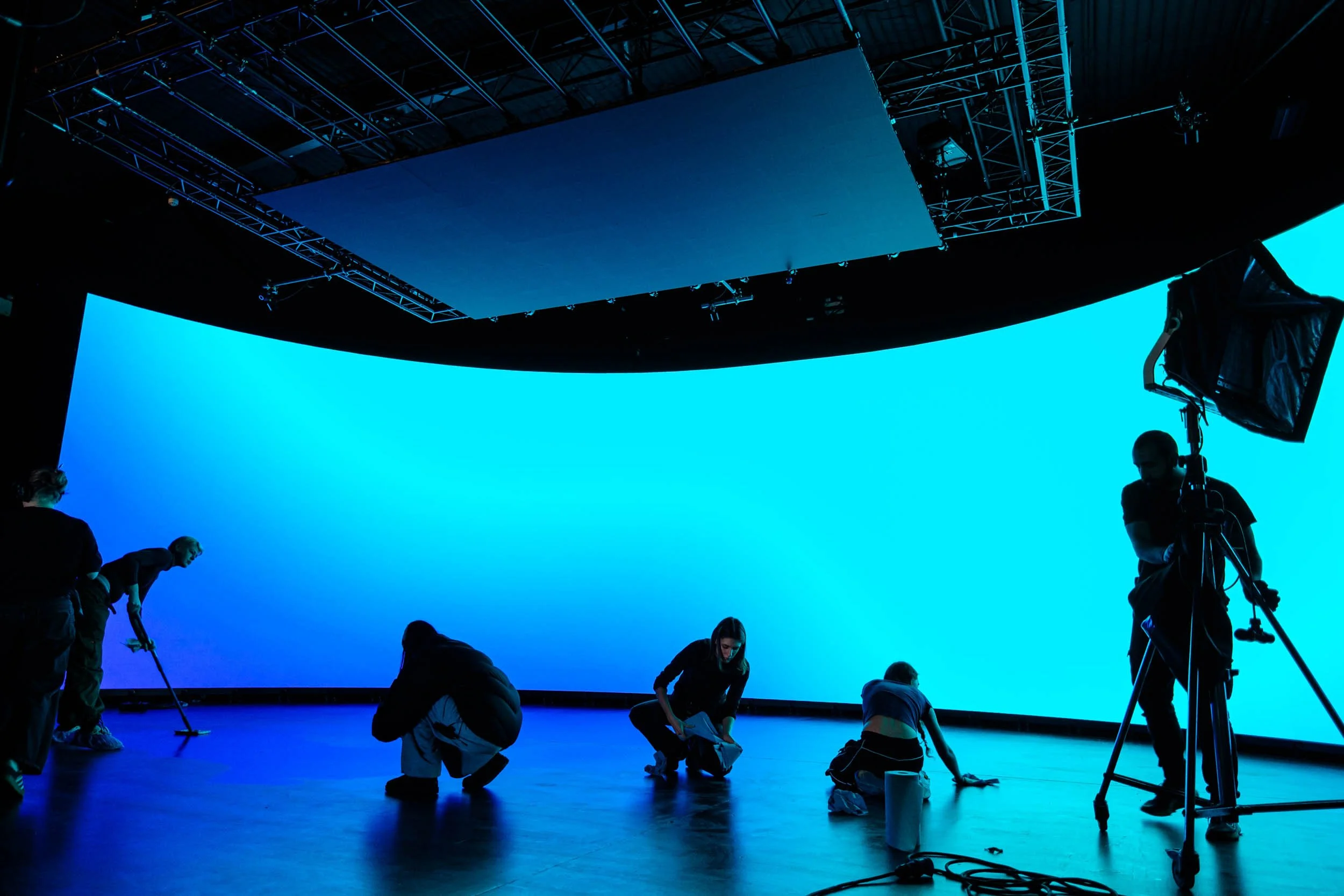 Large curved LED screen and ceiling with an abstract blue gradient light as production team cleans floor ready for next take onset at a shoot for a brand