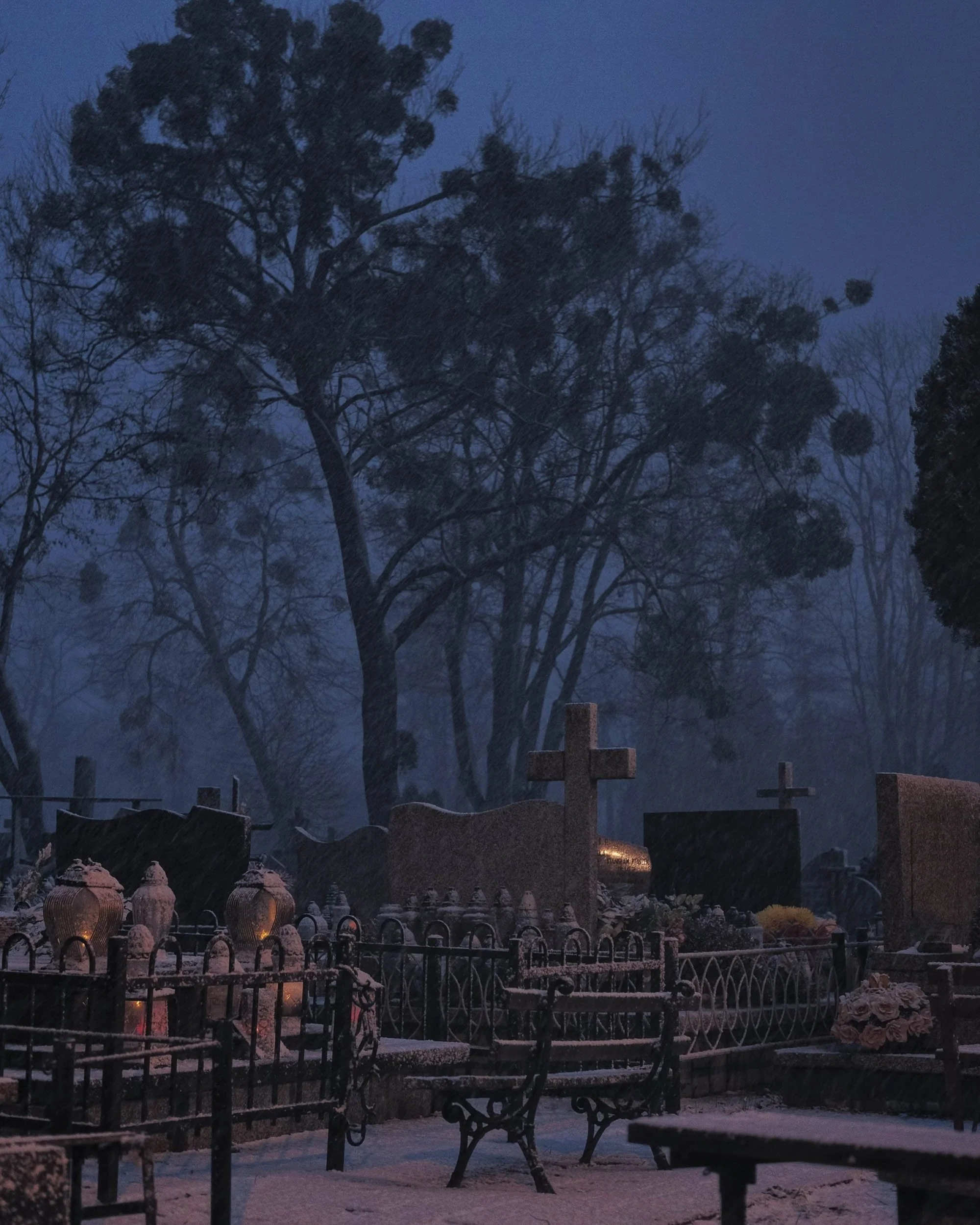 Moody scene of a snow covered cemetery in Zamosc eastern Poland with trees disappearing into the snowy mist lit by the warm glow of street lamps