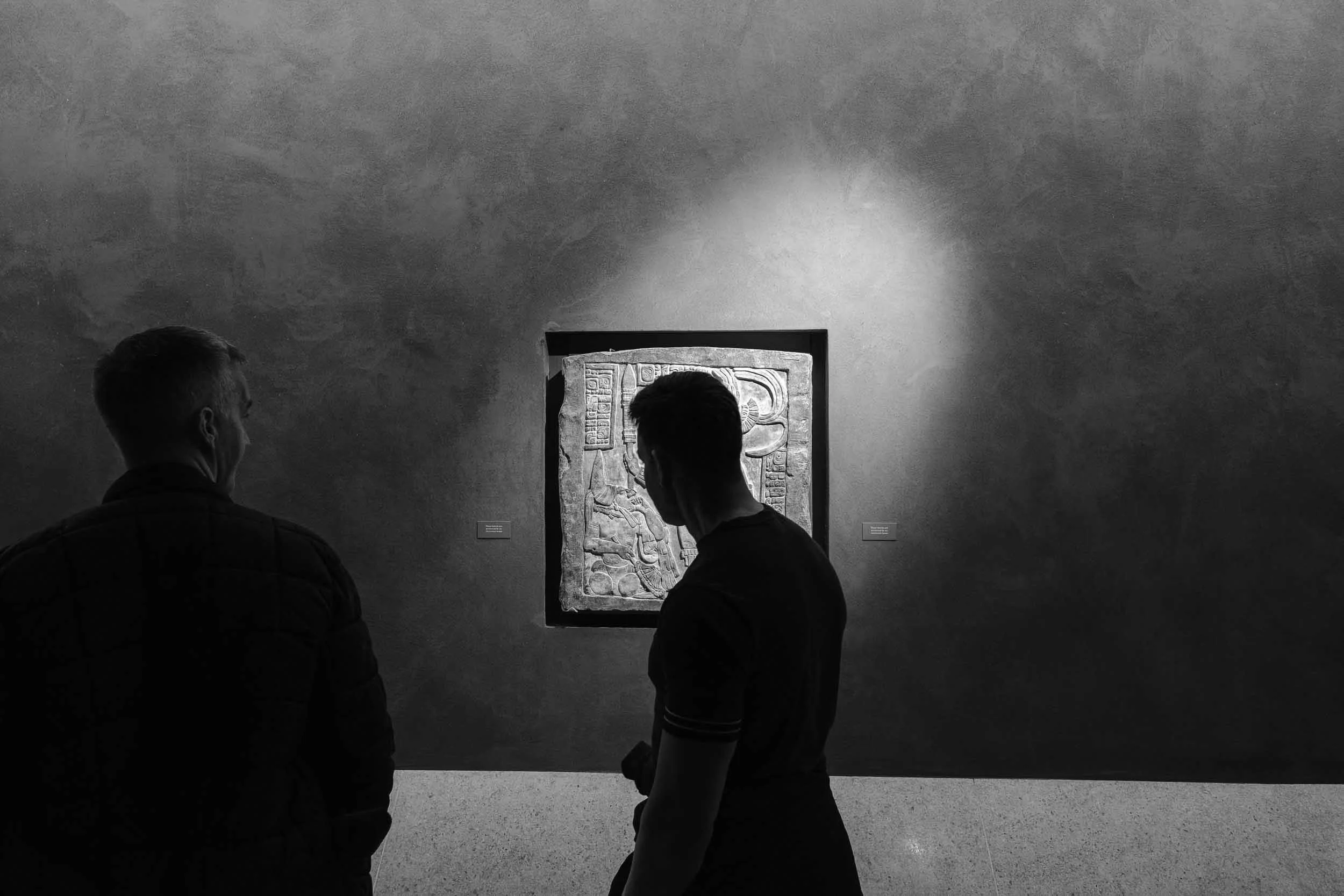 Black and white image of a mans silhouette framed by an artwork in a museum in London