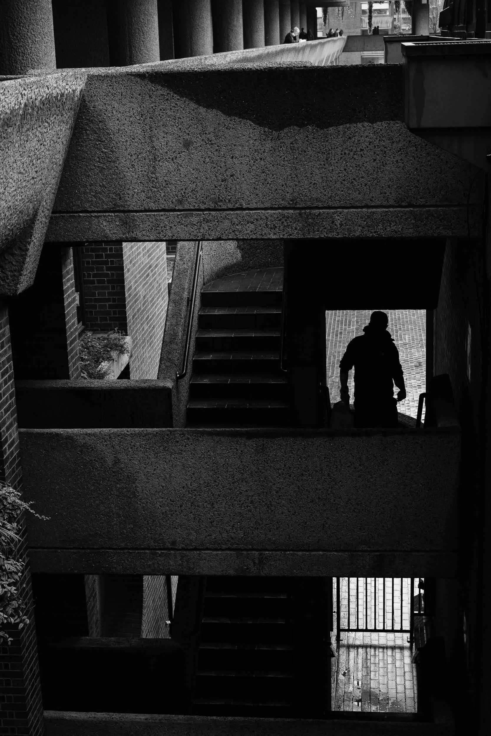 Gritty black and white a man walks down the stairs at the Barbican Centre in London framed up in a single doorway like a noir movie
