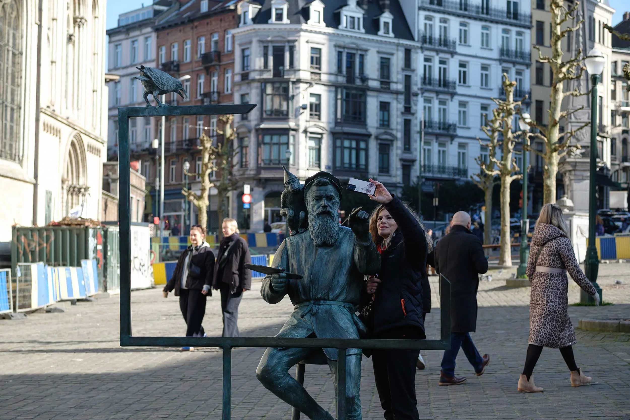 A woman takes a selfie with a famous statue in Brussels on a busy street