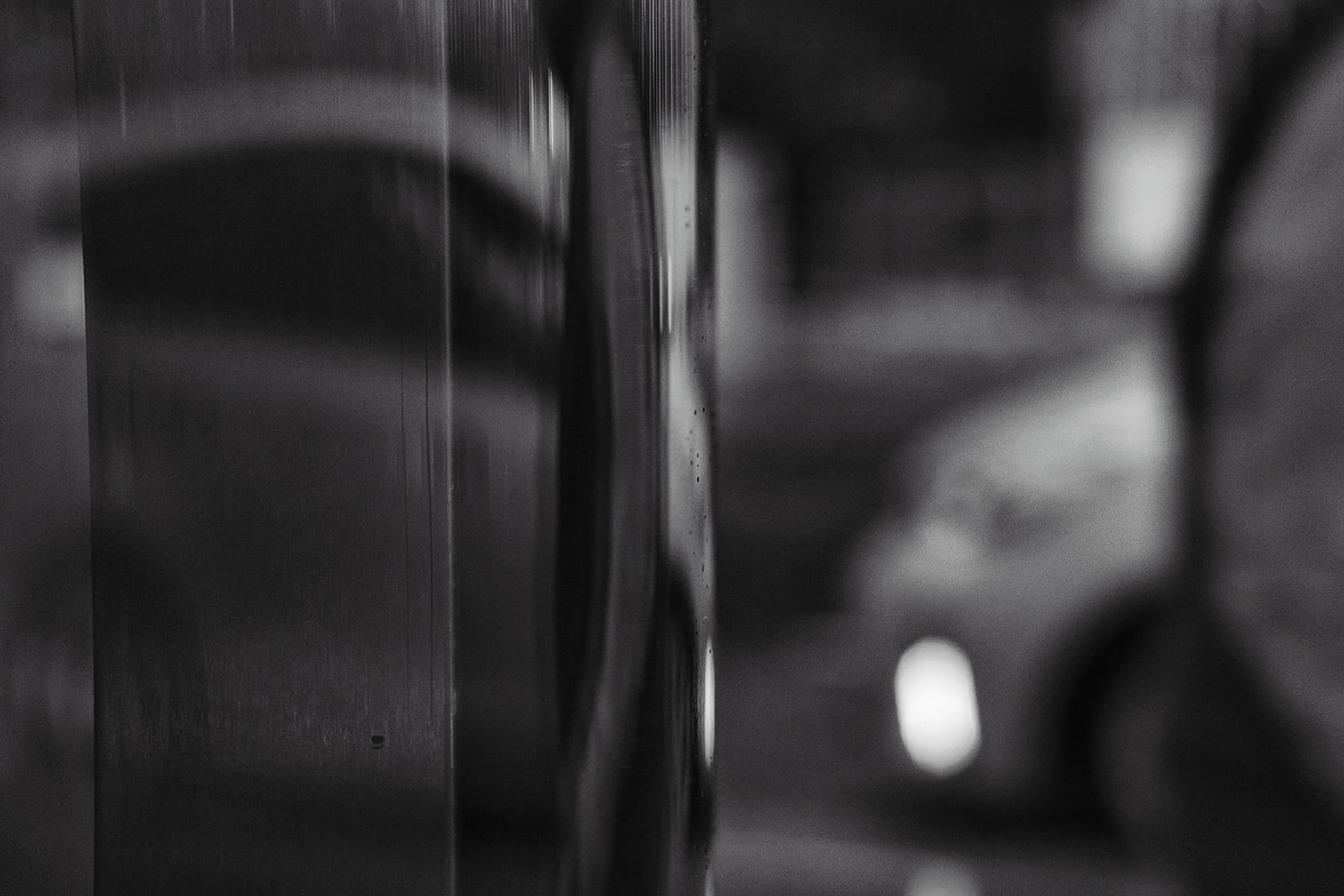 Close-up of a metallic texture with shallow depth of field giving an abstract nature in black and white with cars lights in the background out of focus bokeh