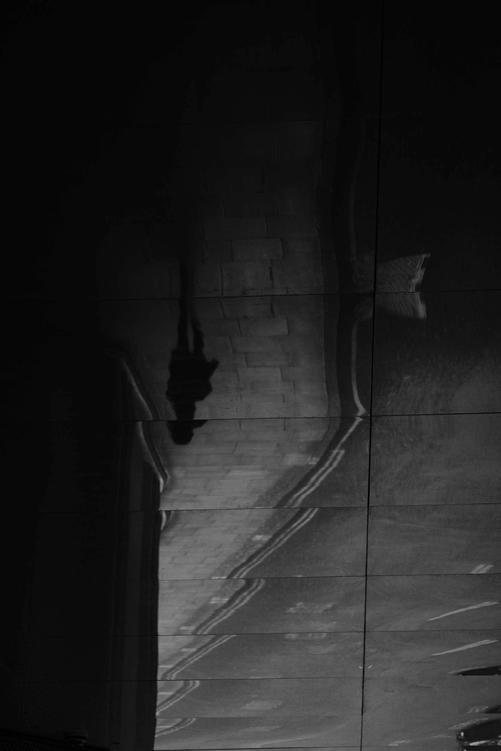 An abstract black and white image of reflections and shadows in the streets of London with a single figure that appears to be walking on the ceiling