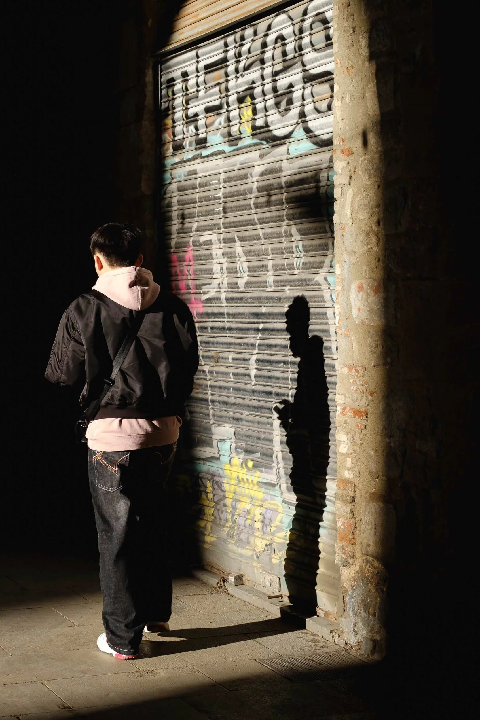 Warm puddle of light cast a mans shadow onto a wall with graffiti and looks like part of the mural in the Gothic Quarter in Barcelona