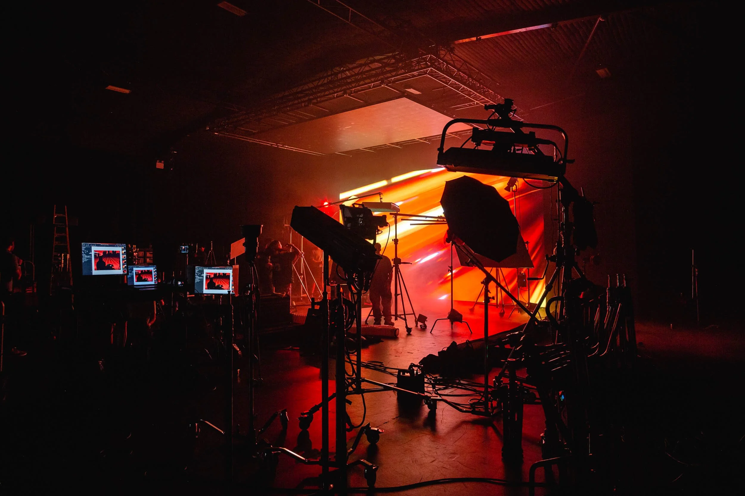 Behind the scenes at a brand shoot for watch brand Tissot with multiple monitors and lighting stands as silhouettes set in front of large LED display casting a deep red colour across the scene