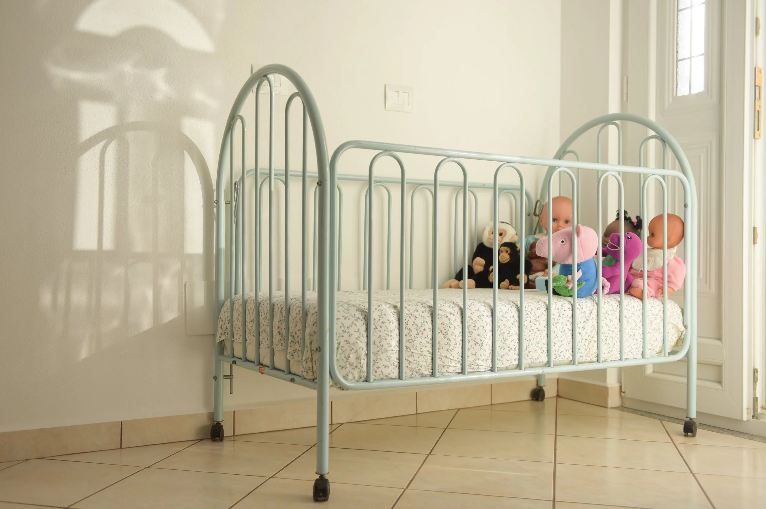 Letto con sbarre blu, appeso a una parete bianca con alcuni giocattoli, tra cui bambole e peluche.