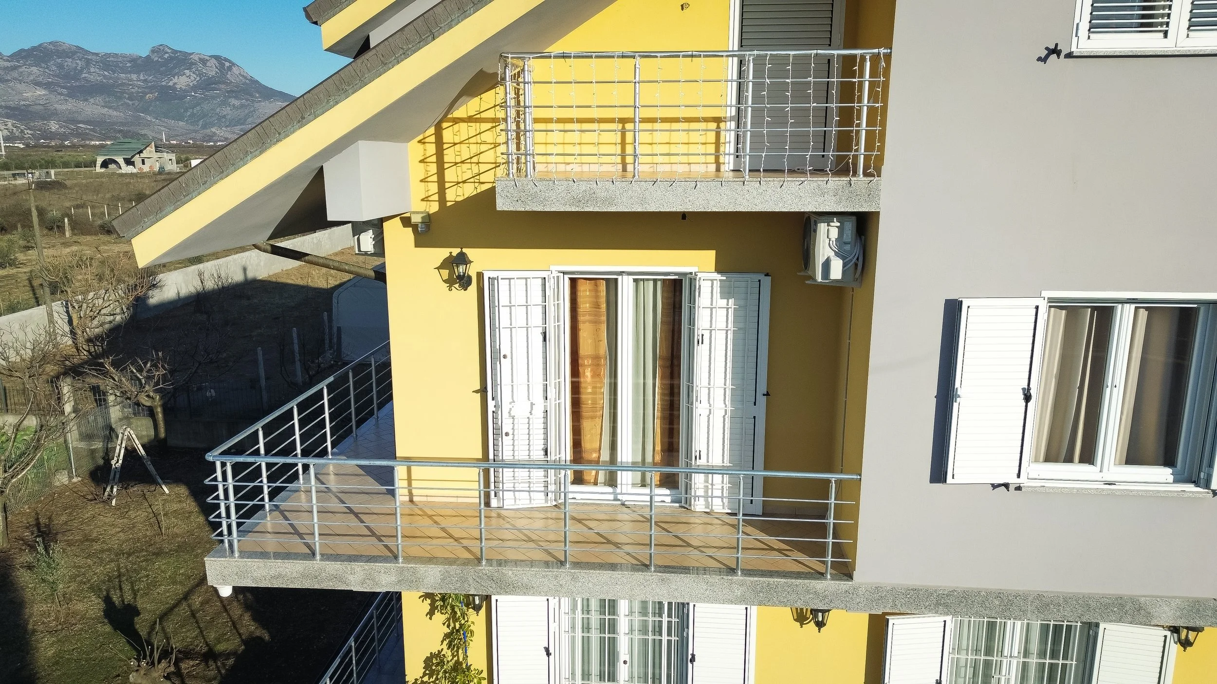 Balcone di un appartamento con ringhiera metallica, finestre con persiane bianche e aria condizionata esterna sulla parete.