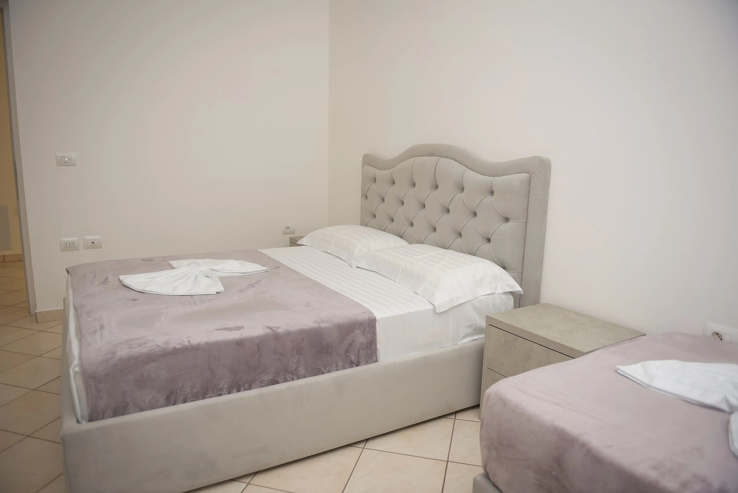 Camera da letto con due letti, testiere imbottite chiare e lenzuola bianche, pareti bianche e mobili color crema.