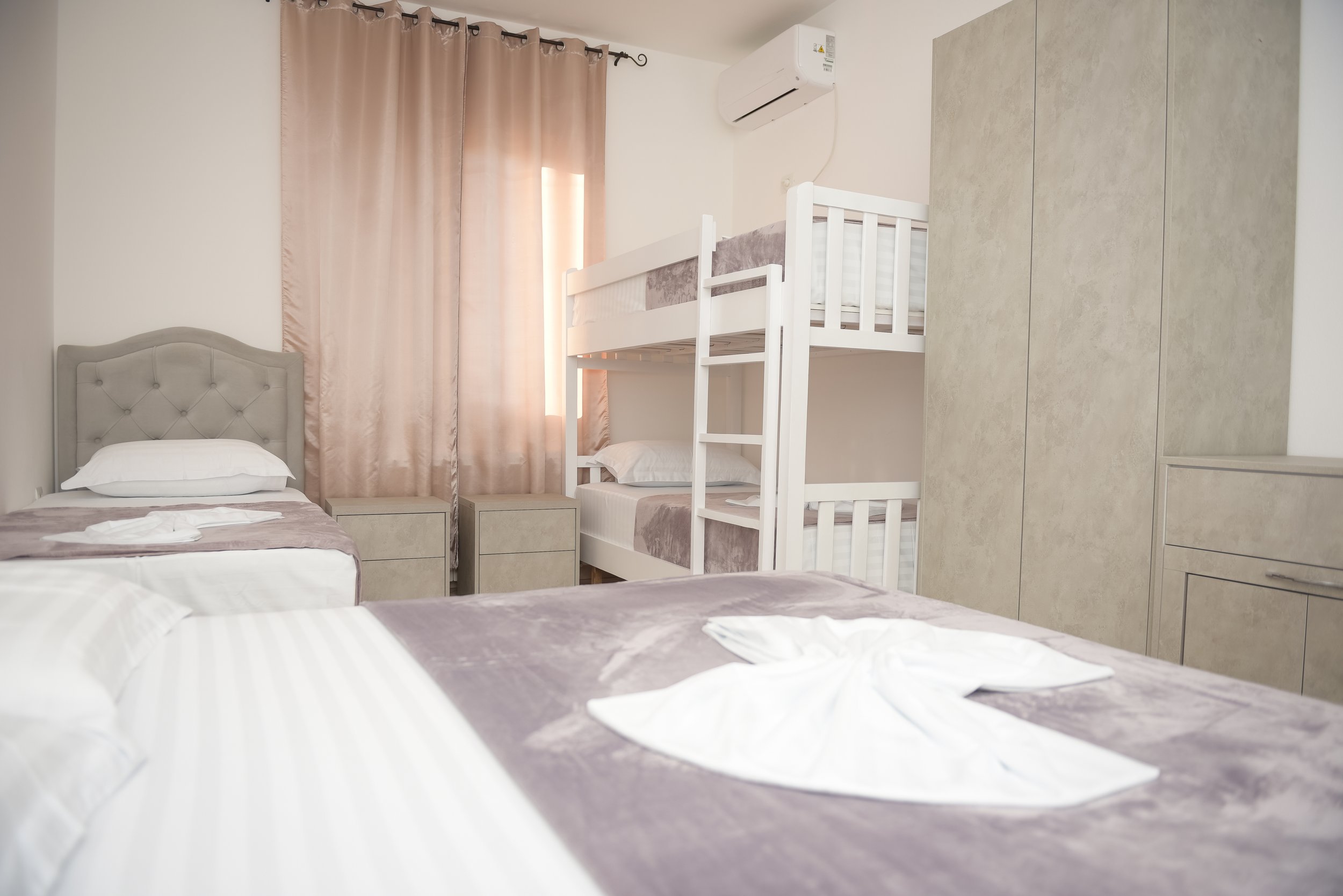 Camera da letto con letti singoli, cuscini e biancheria, tende beige e aria condizionata.
